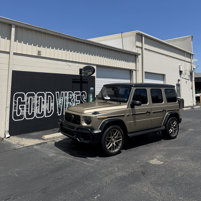 Tan SUV parked outside a beige building with a black mural reading “GOODW...”