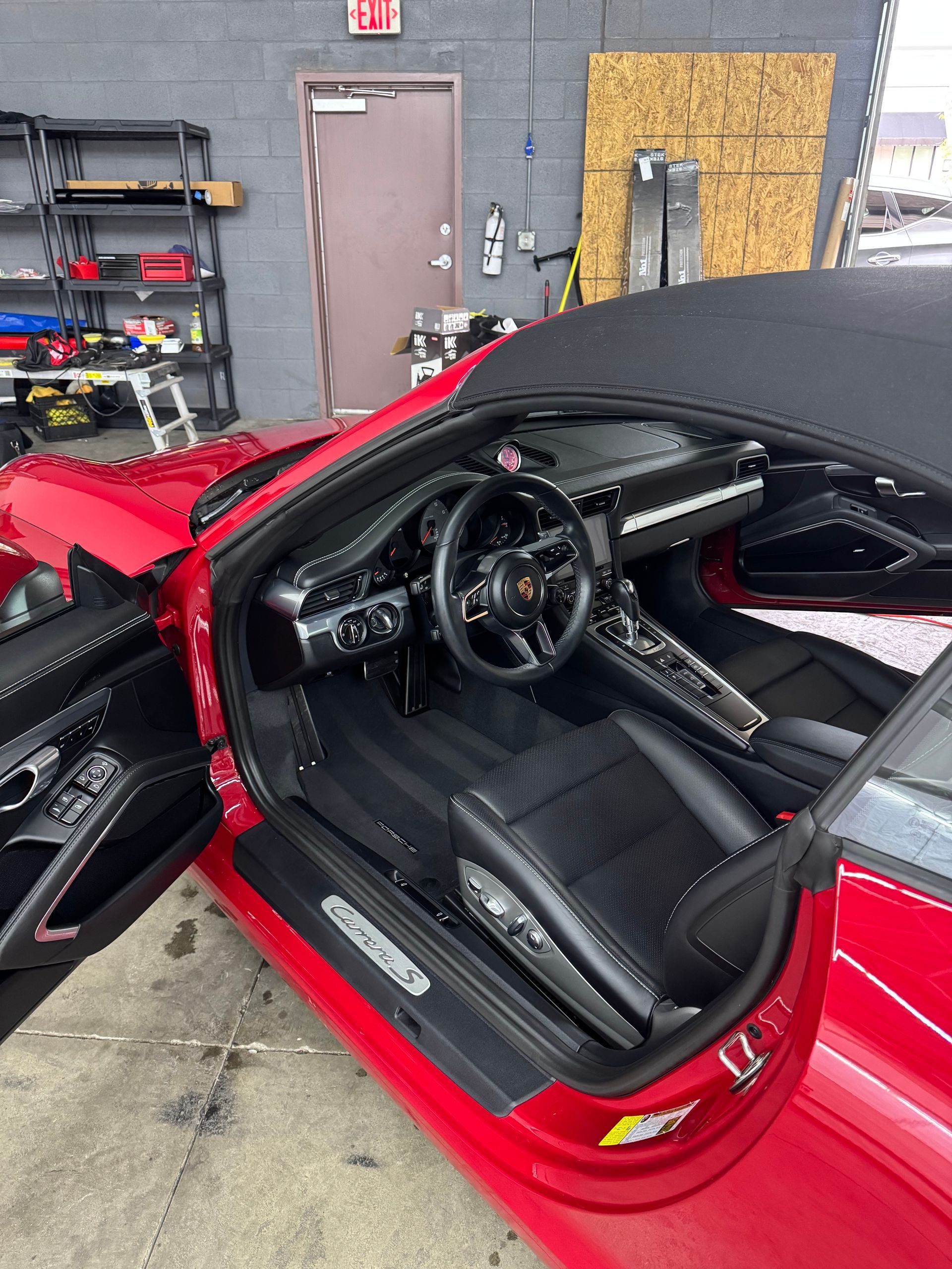 Red convertible car interior with black leather seats, door open. Garage setting.