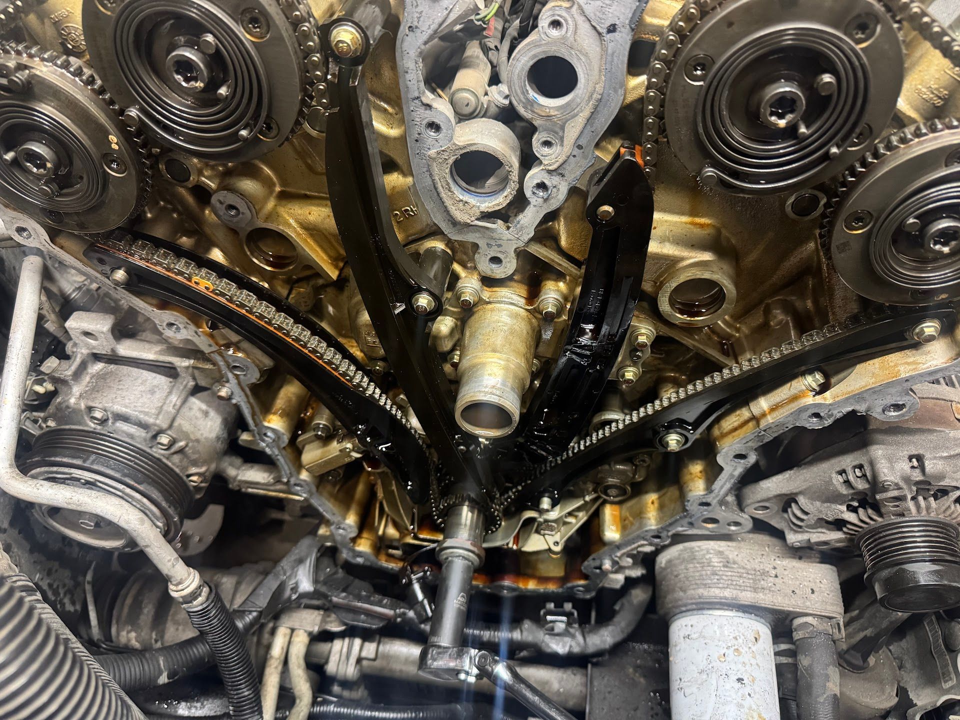 Inside an open car engine, showing timing chains, gears, and black guide rails coated in oil. | G Tech Repair