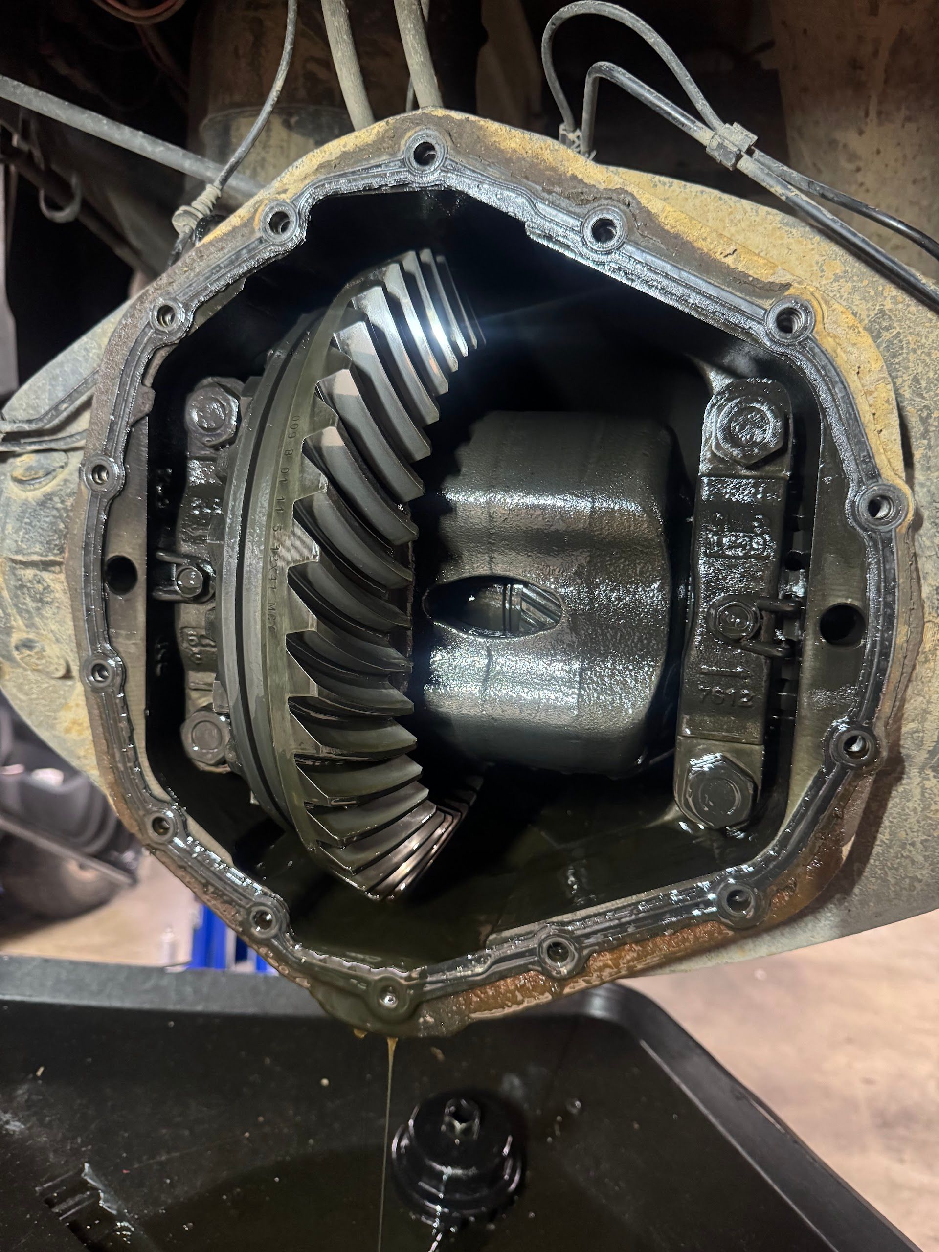 The open differential of a vehicle with dark oil draining into a collection pan below. | G Tech Repair