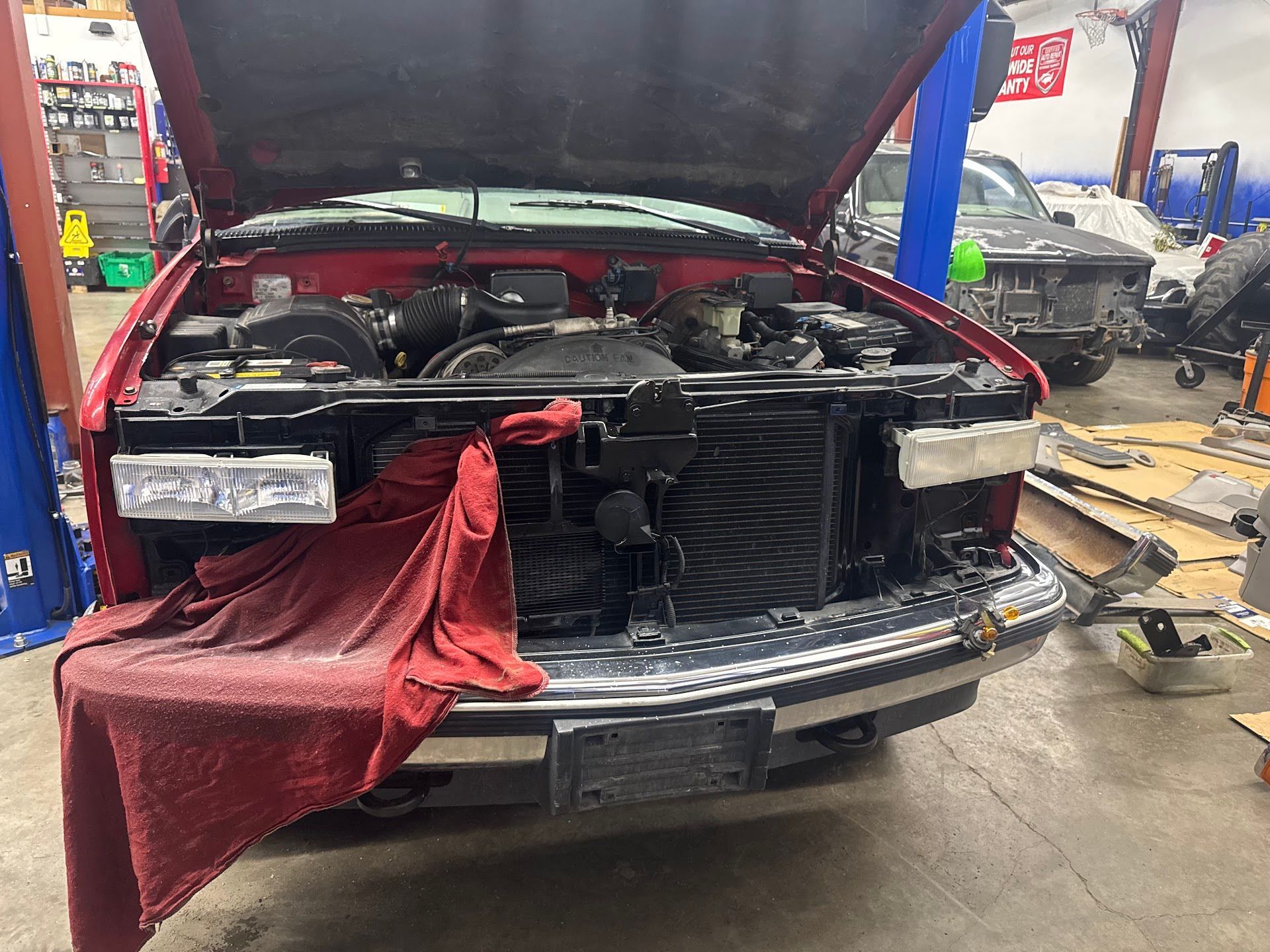 A red truck with its hood open and a red shop towel draped over the front bumper inside an auto repair shop. | G Tech Repair