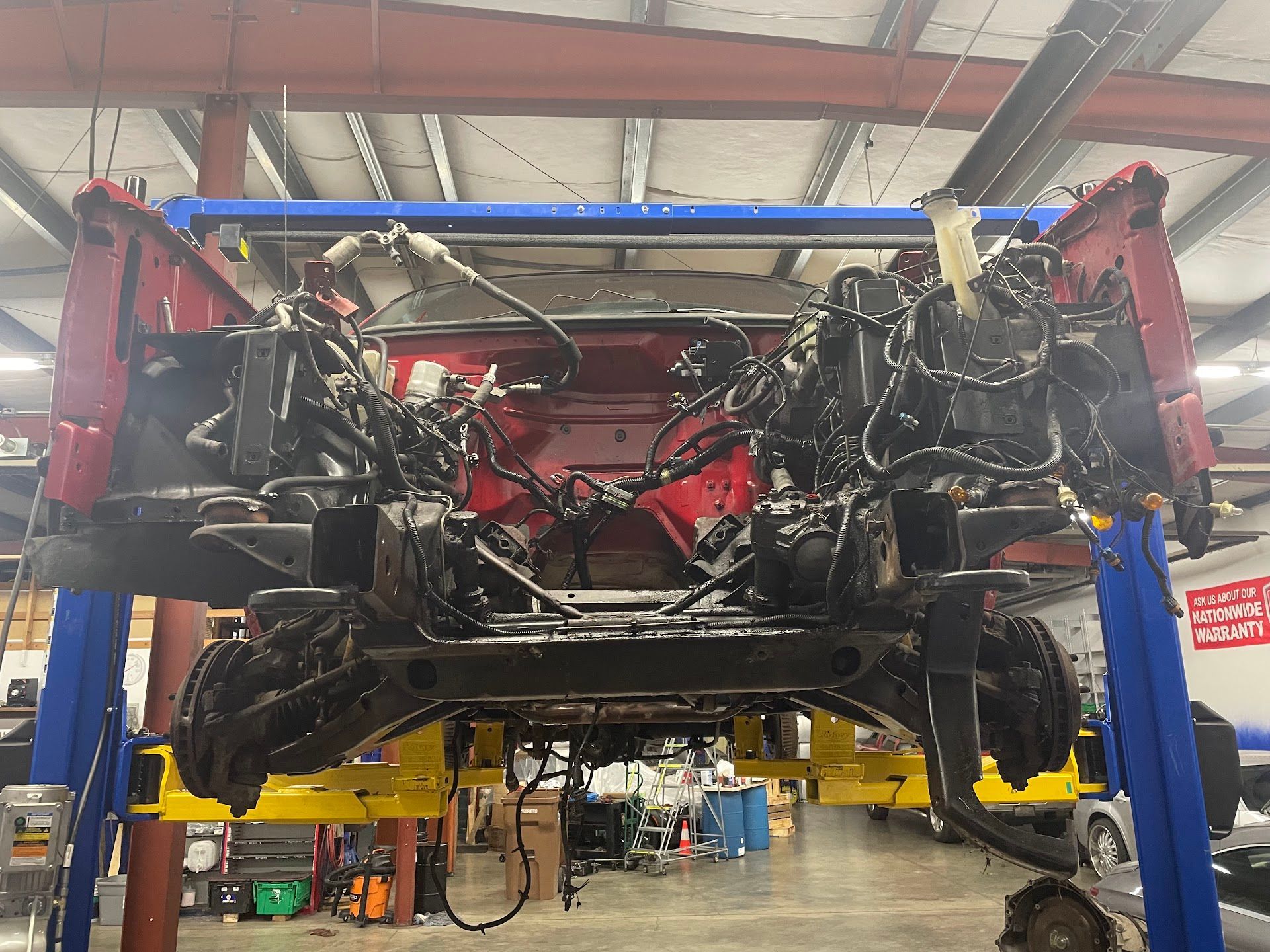 An automotive chassis, missing its engine, is suspended on a yellow hydraulic lift inside a workshop. | G Tech Repair