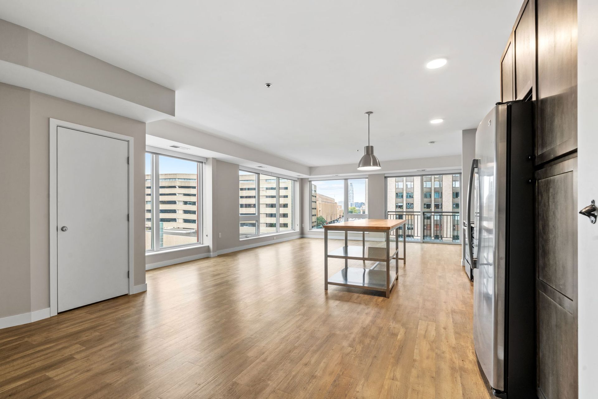 An open-concept living area with light wood floors, large windows, a kitchen island, and stainless steel appliances.