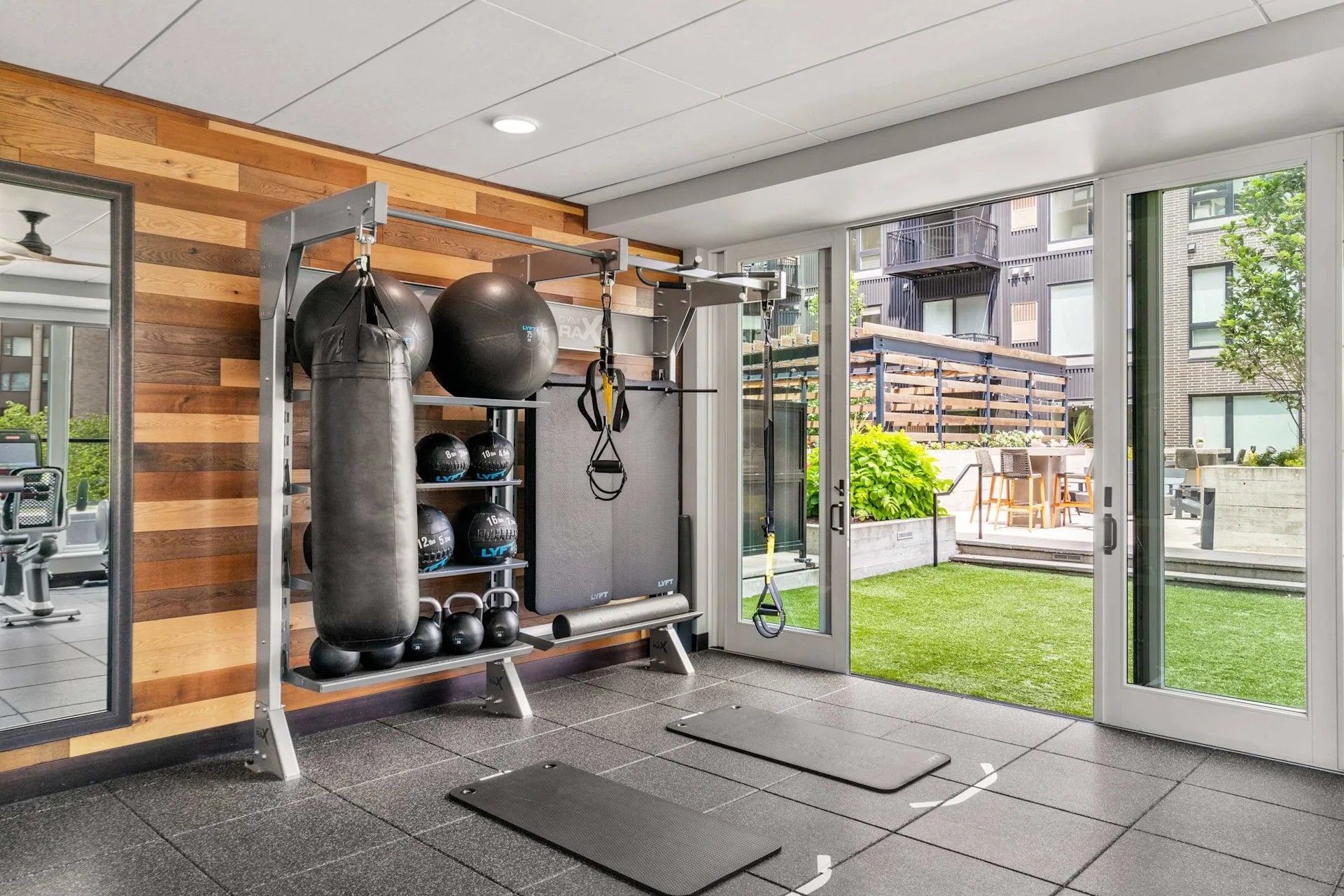 Modern home gym with a boxing bag, fitness equipment, and workout mats, opening onto a backyard patio through glass doors.