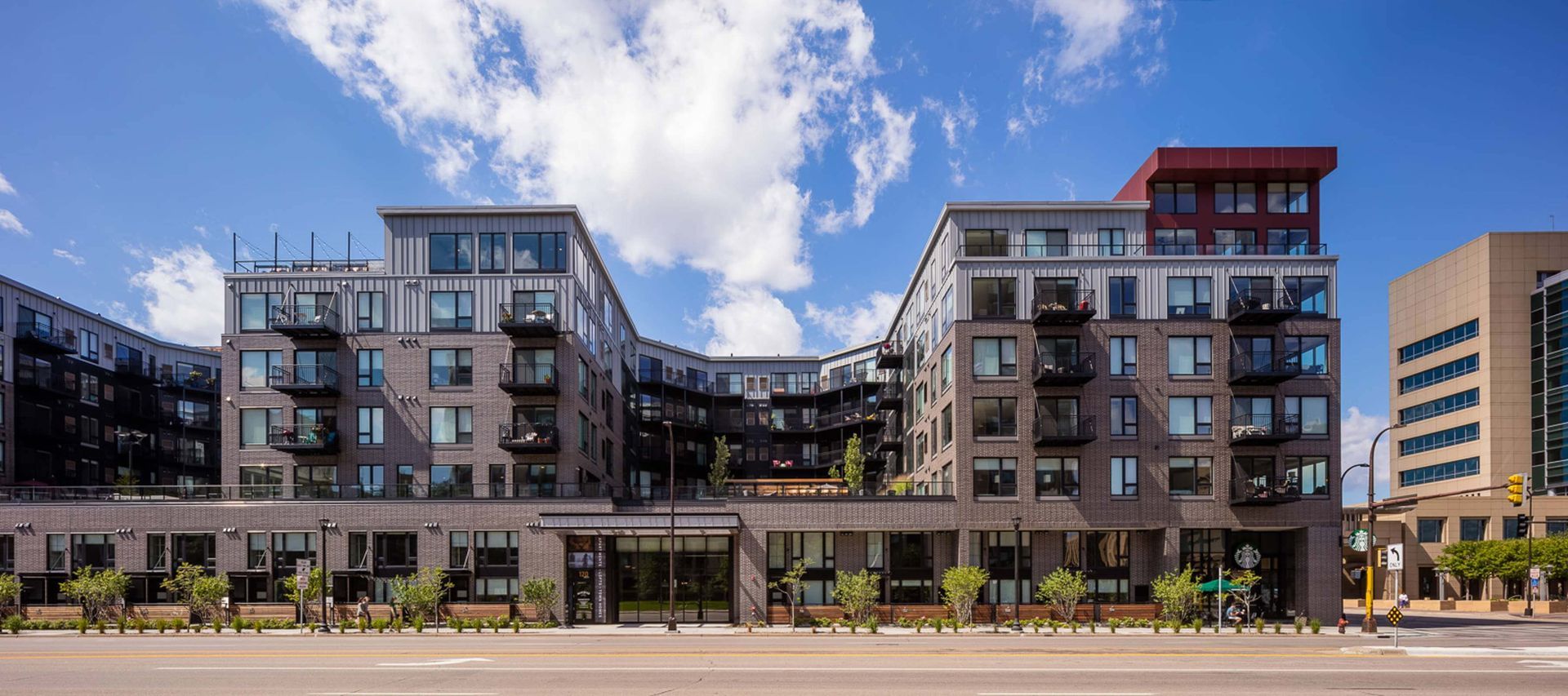 A modern, U-shaped apartment complex with gray brick and light gray siding under a bright blue sky.