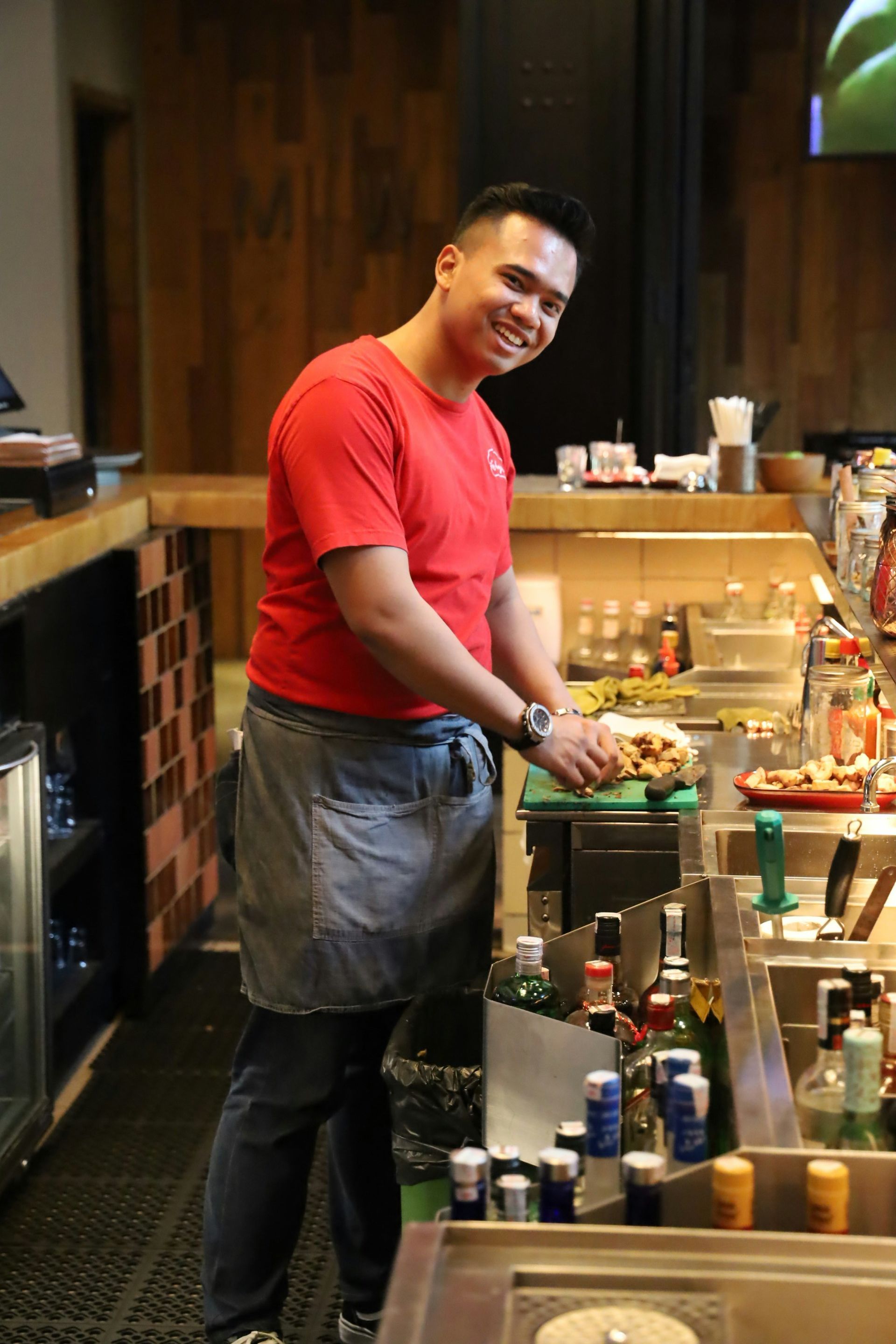A man in a red shirt is standing in a kitchen preparing food.