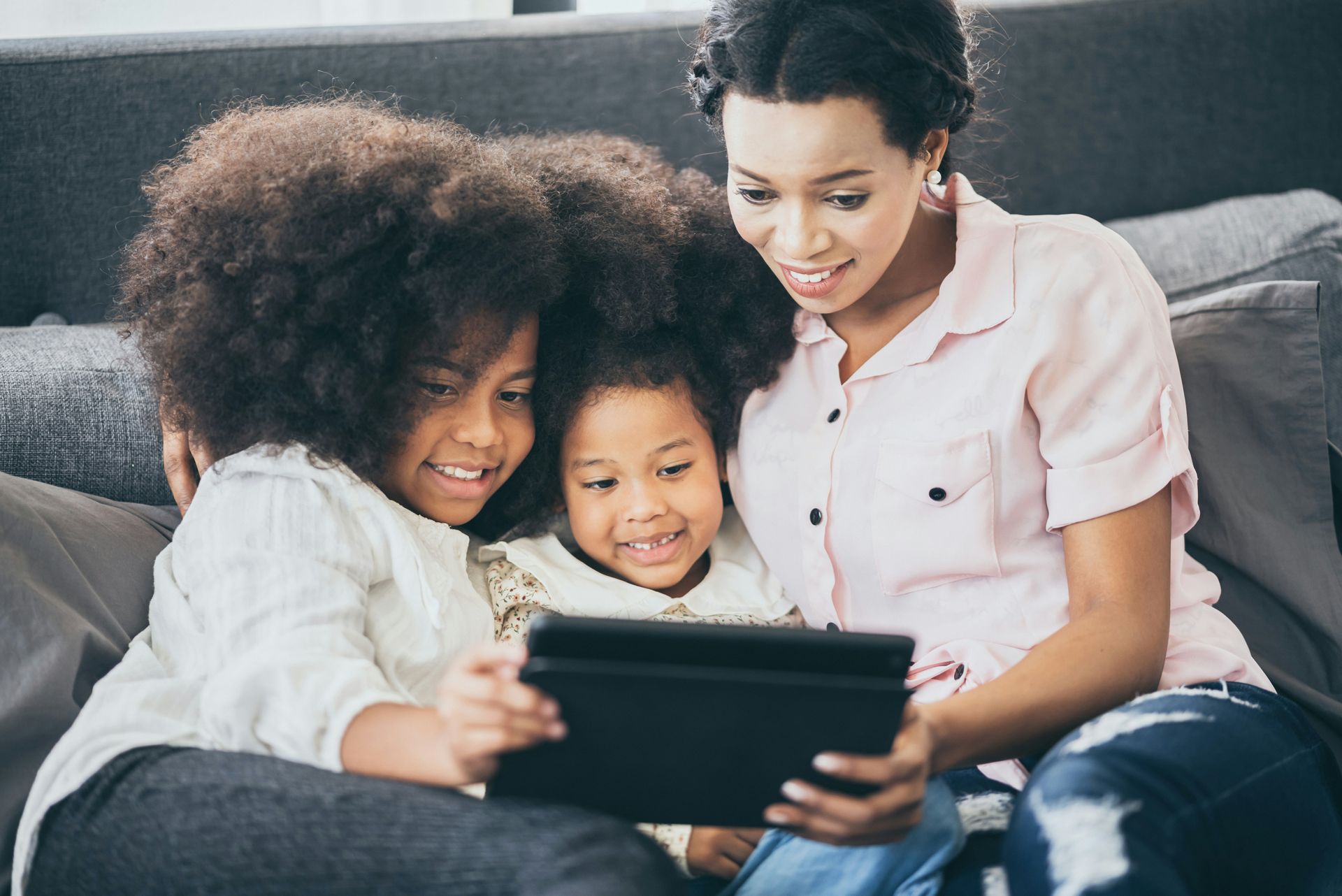 A woman and two children are sitting on a couch looking at a tablet.