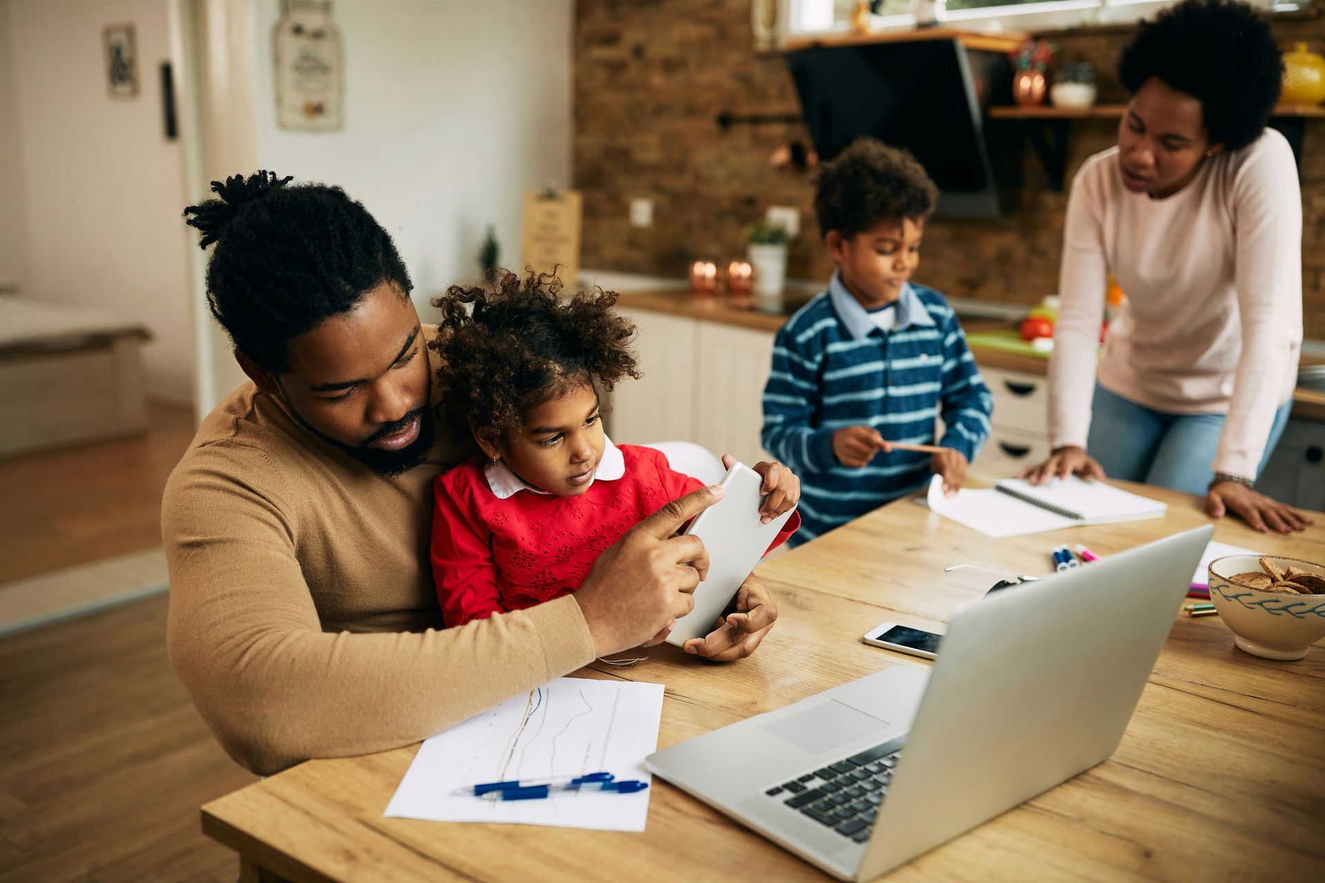 A family is sitting at a table with a laptop and a tablet.