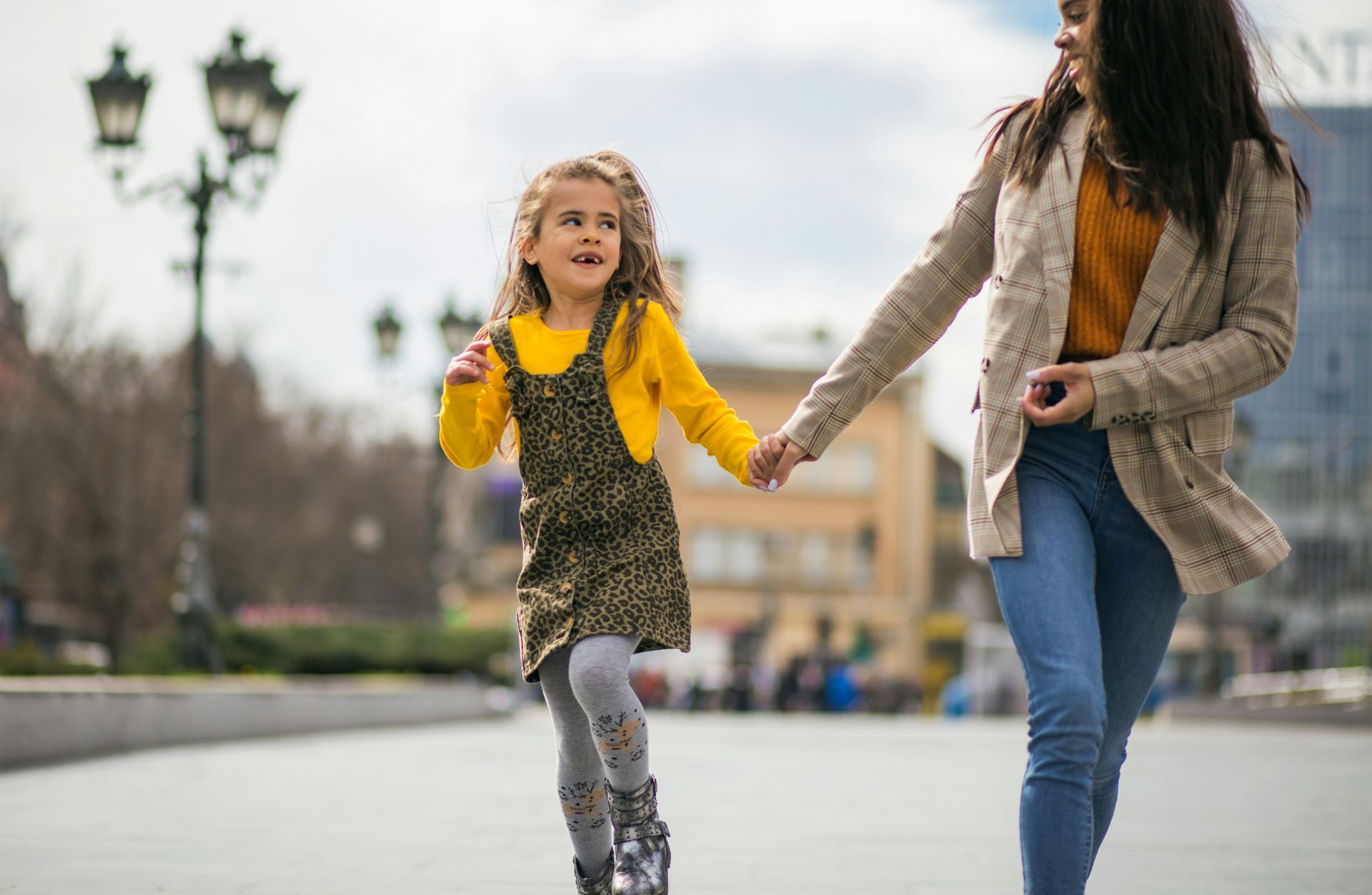 A woman and a little girl are holding hands while walking down the street.