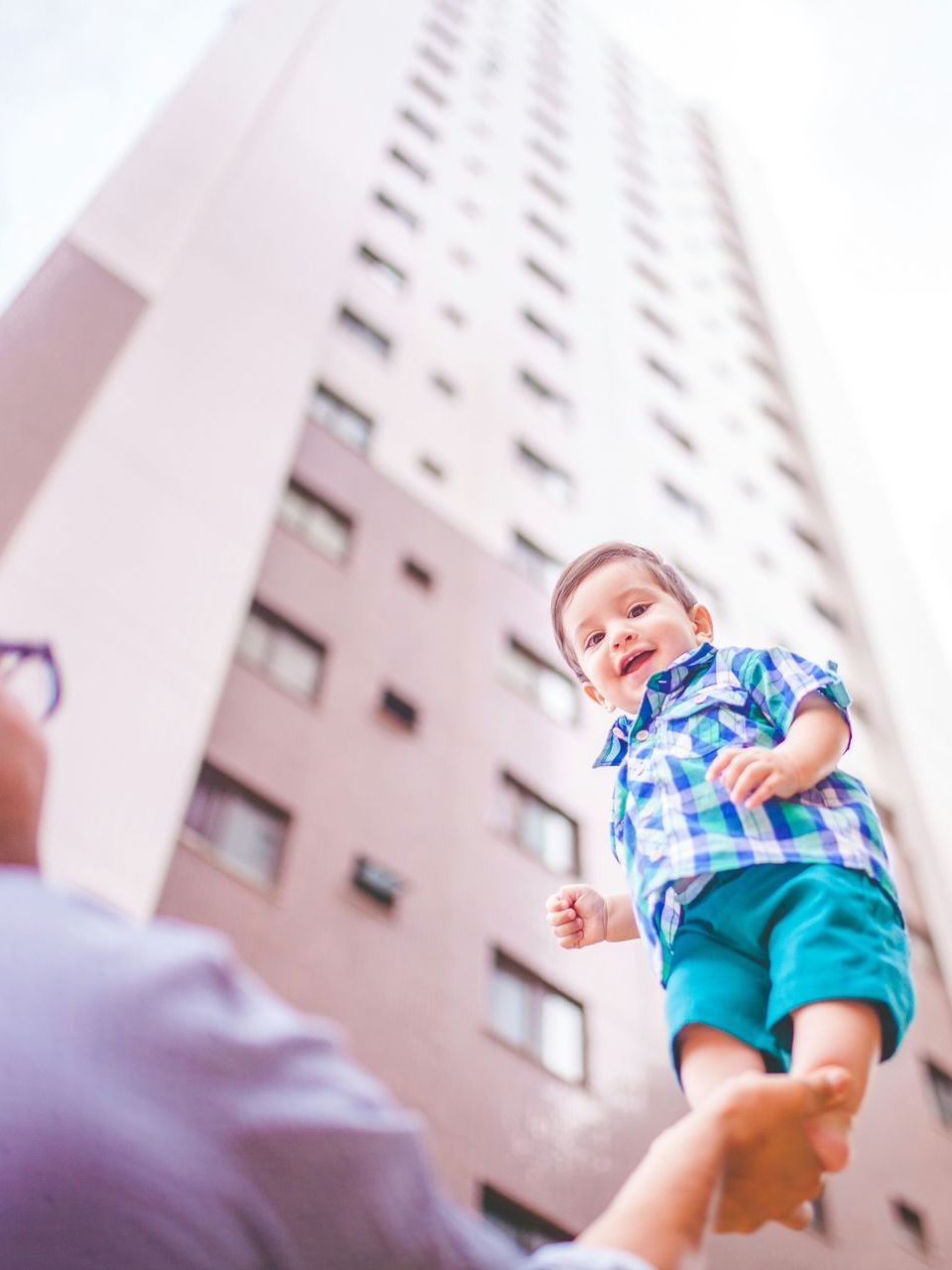 A baby is being held up in the air by a man in front of a tall building.