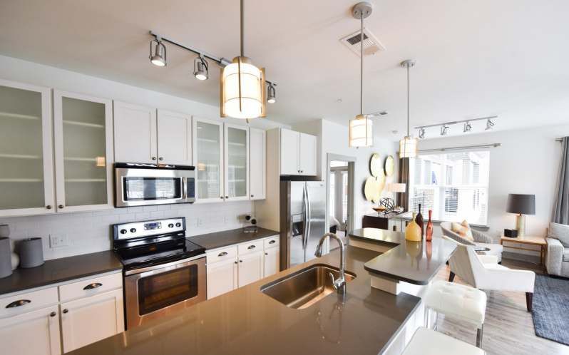 Modern white kitchen with stainless steel appliances, island, and open living area.