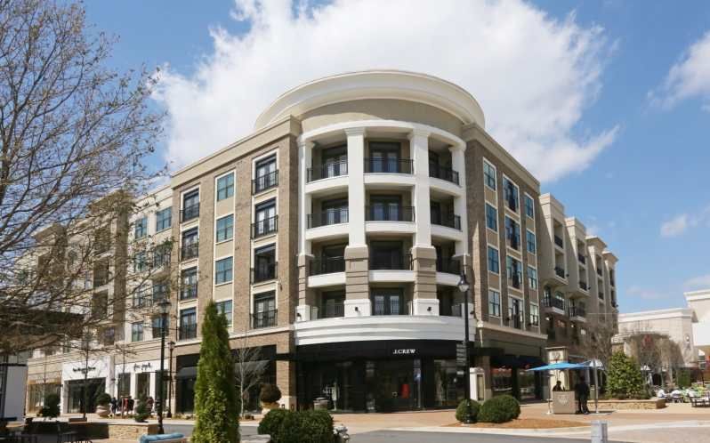 Multi-story building with stores on the bottom and apartments above, under a bright blue sky with puffy clouds.