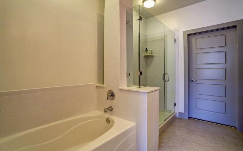 Bathroom with white tub, glass shower, and grey door.