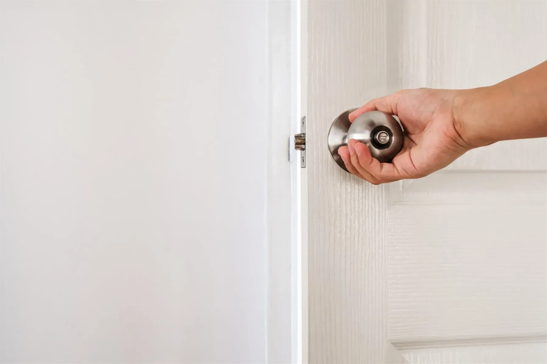 A Person Is Holding a Door Knob and Opening a White Door — Lock & Door in Wodonga, VIC