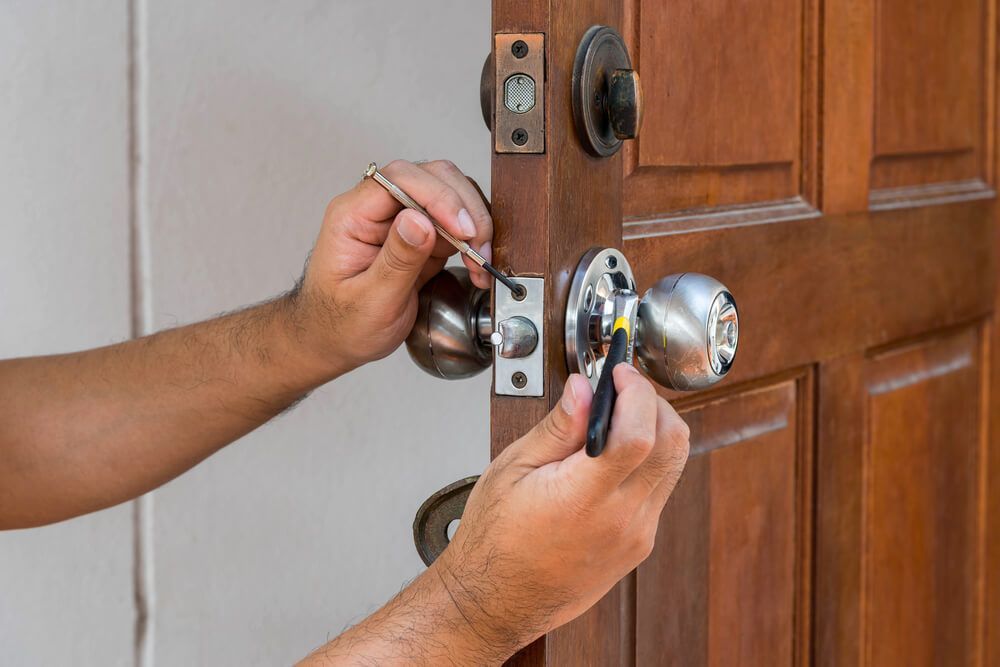 A Man Is Fixing a Door Knob with A Screwdriver — Lock & Door in Albury, NSW