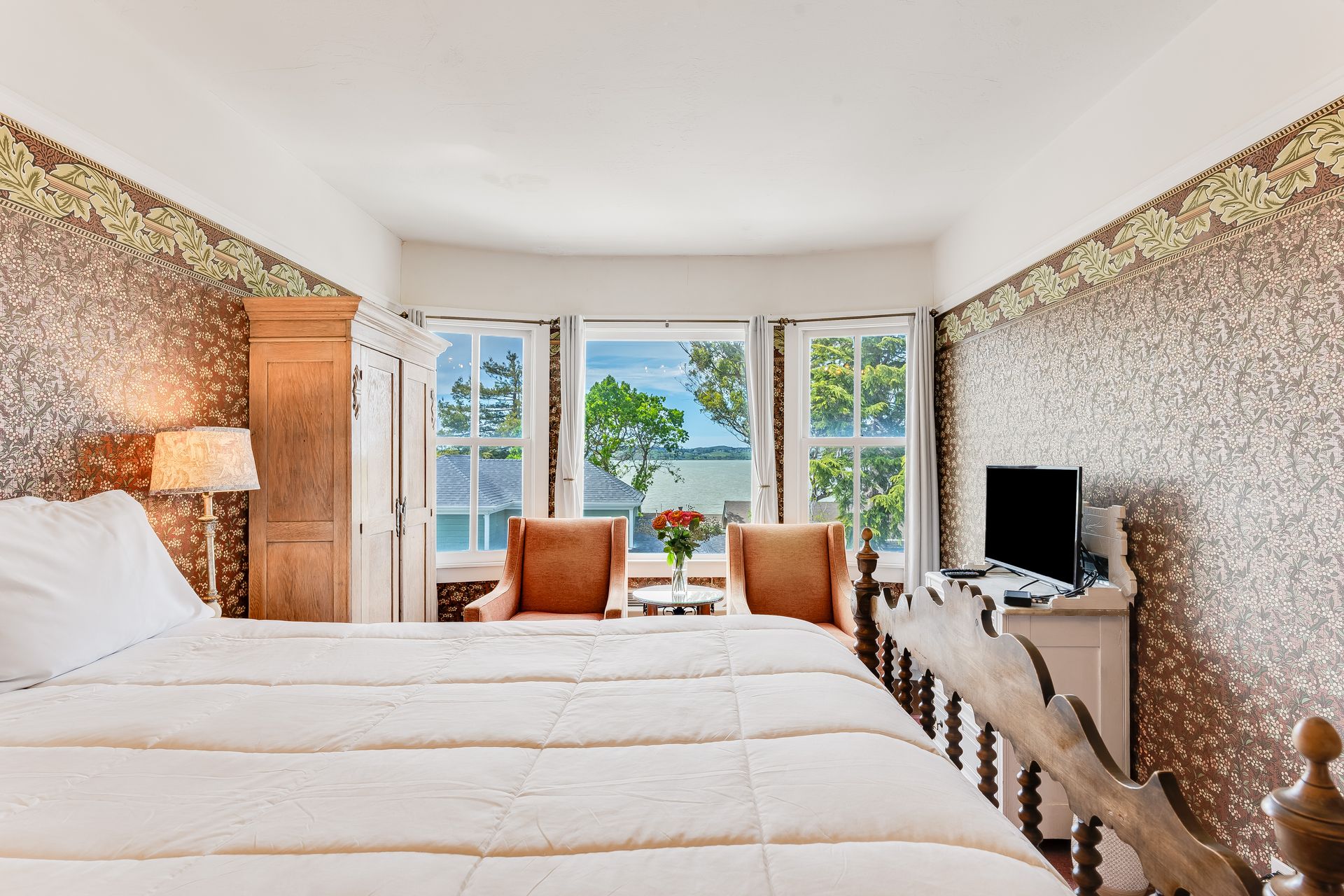 Bedroom with bed, armchairs, and window overlooking water.