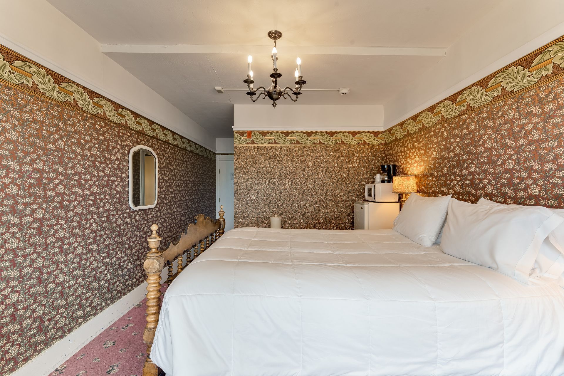 Bedroom with a king bed, floral wallpaper, small mirror, and a microwave.