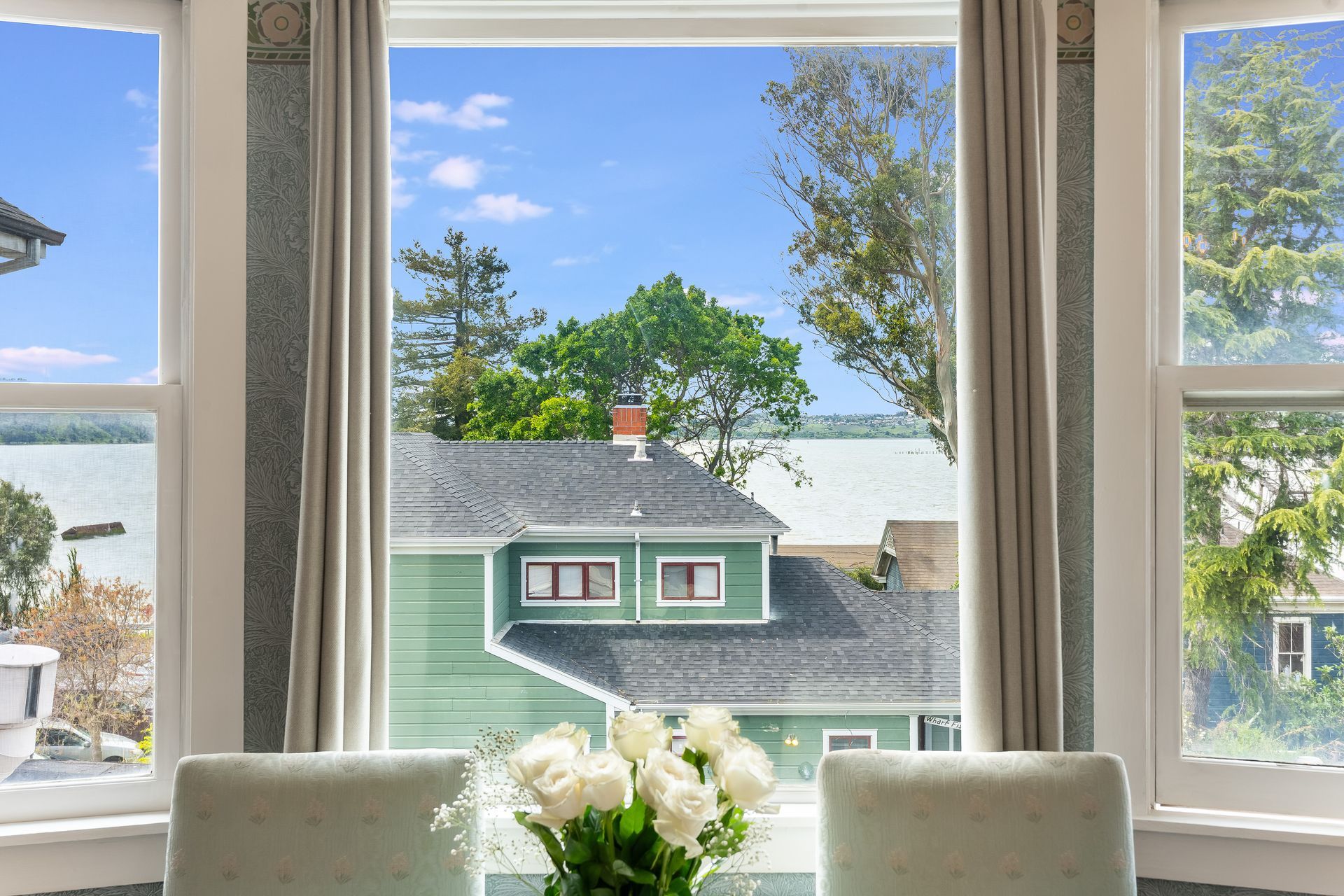 View from a window: A green house roof with a blue sky and water in the background.