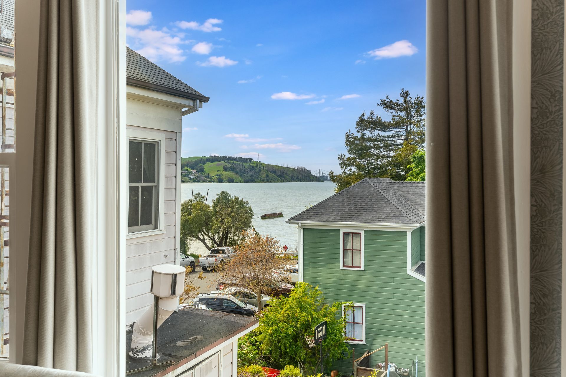 View through a window: waterfront homes, water, and a bridge on a sunny day.