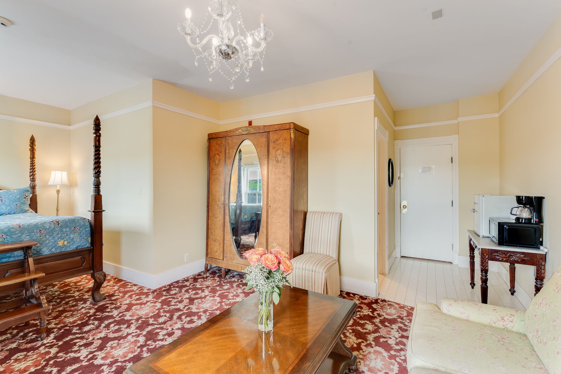 Hotel room with four-poster bed, antique wardrobe, seating area, and a small table with coffee maker.