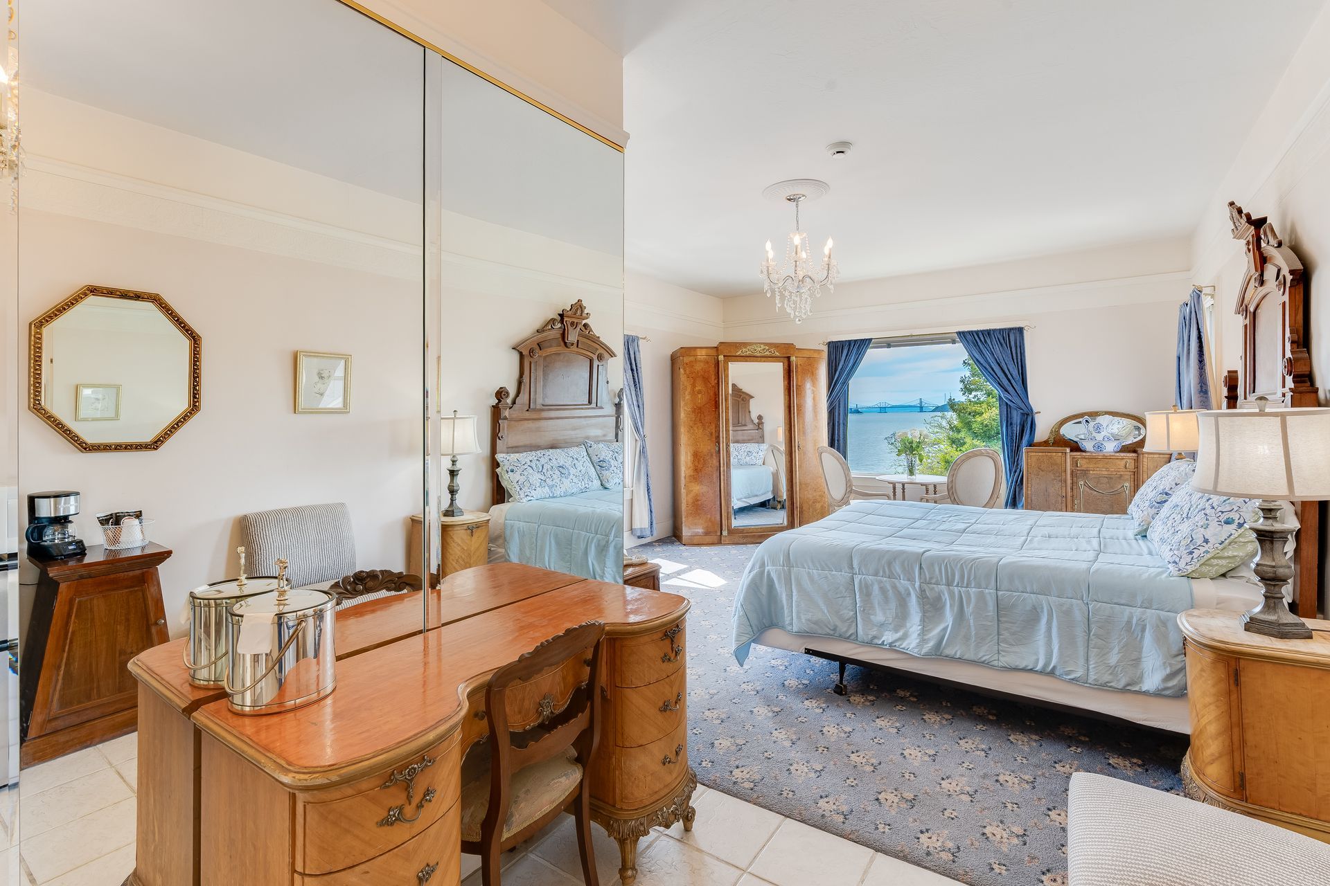 Bedroom with antique furniture, large mirror, blue and white decor, and a view of the water.