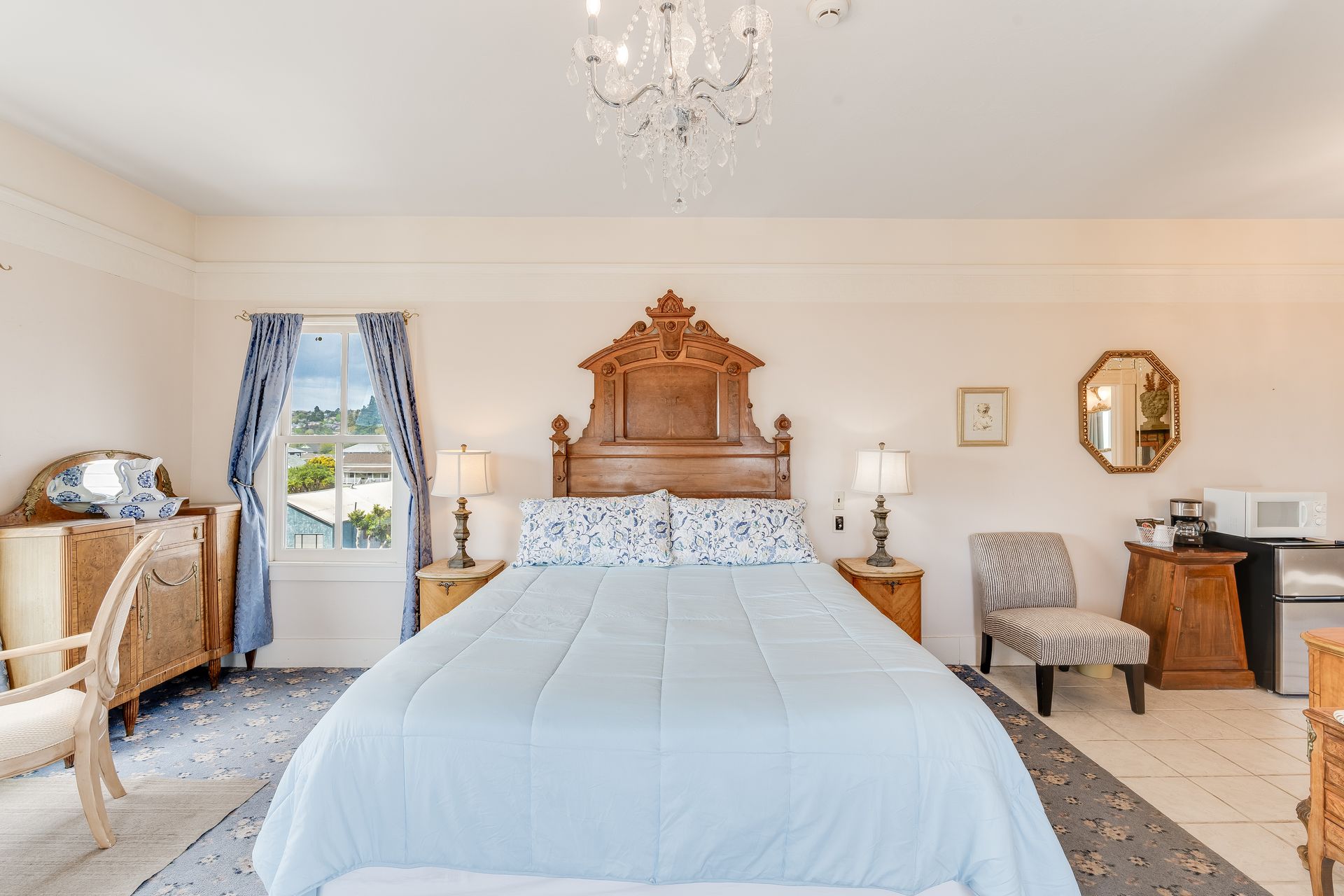 Bedroom with a large bed, antique furniture, and a chandelier. Light blue and wooden accents.