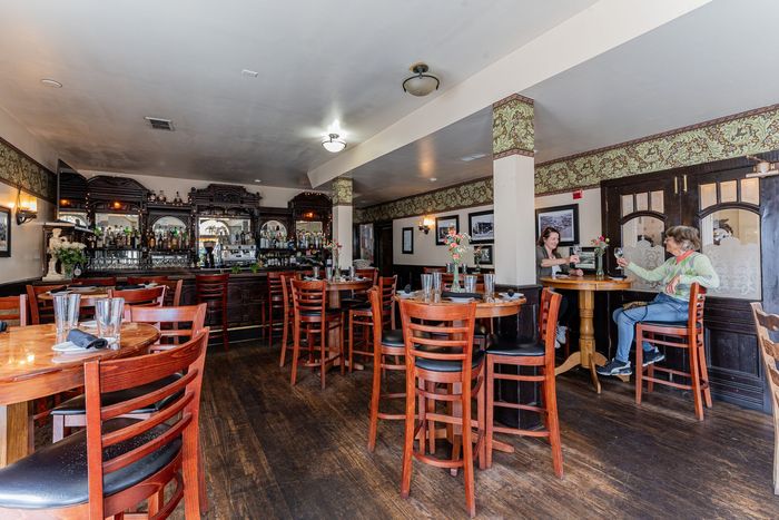Interior view of a pub with tables, chairs, and a bar; a person sits at a table.