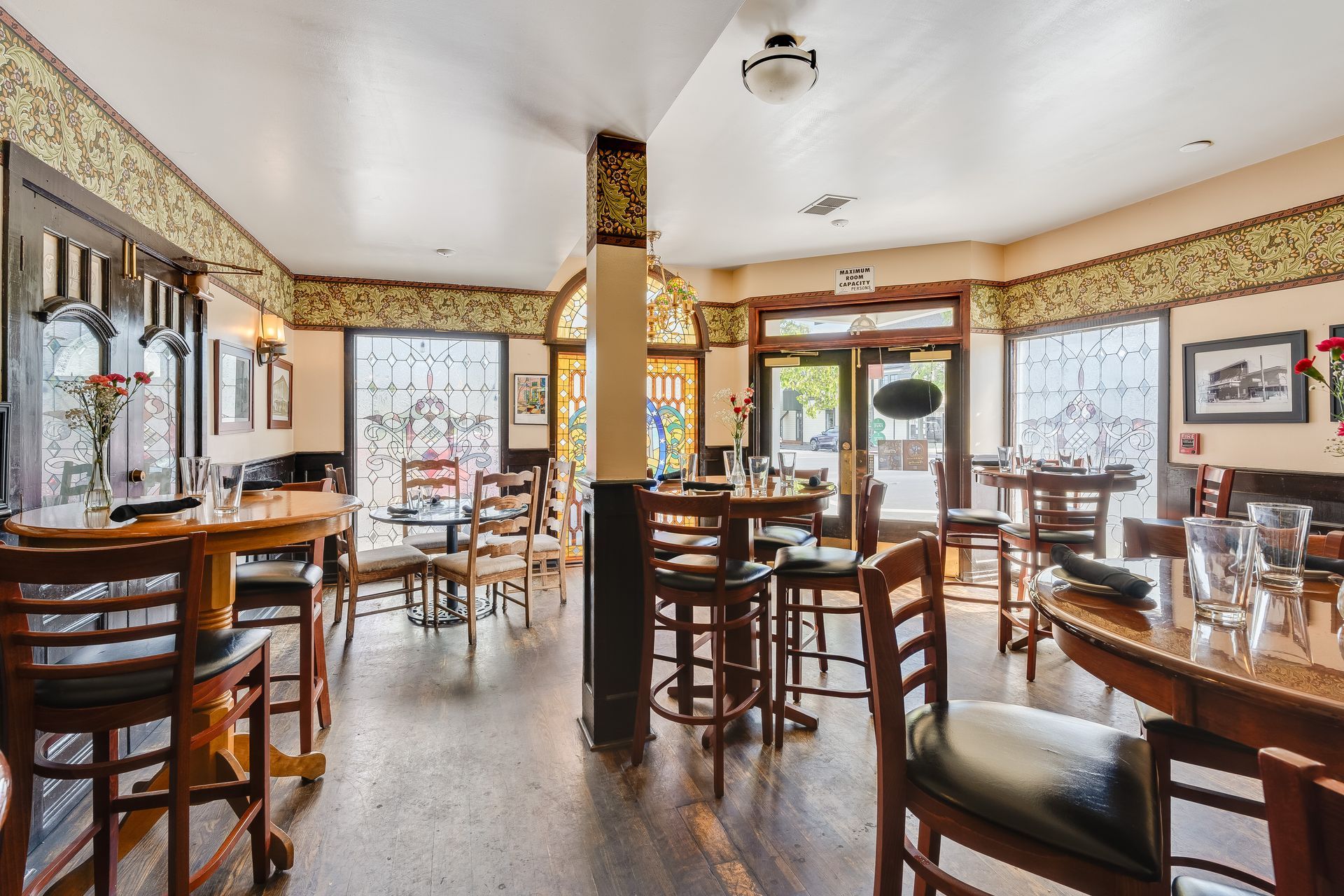 Interior of a restaurant with wooden tables and chairs. Natural light shines through windows and the open door.