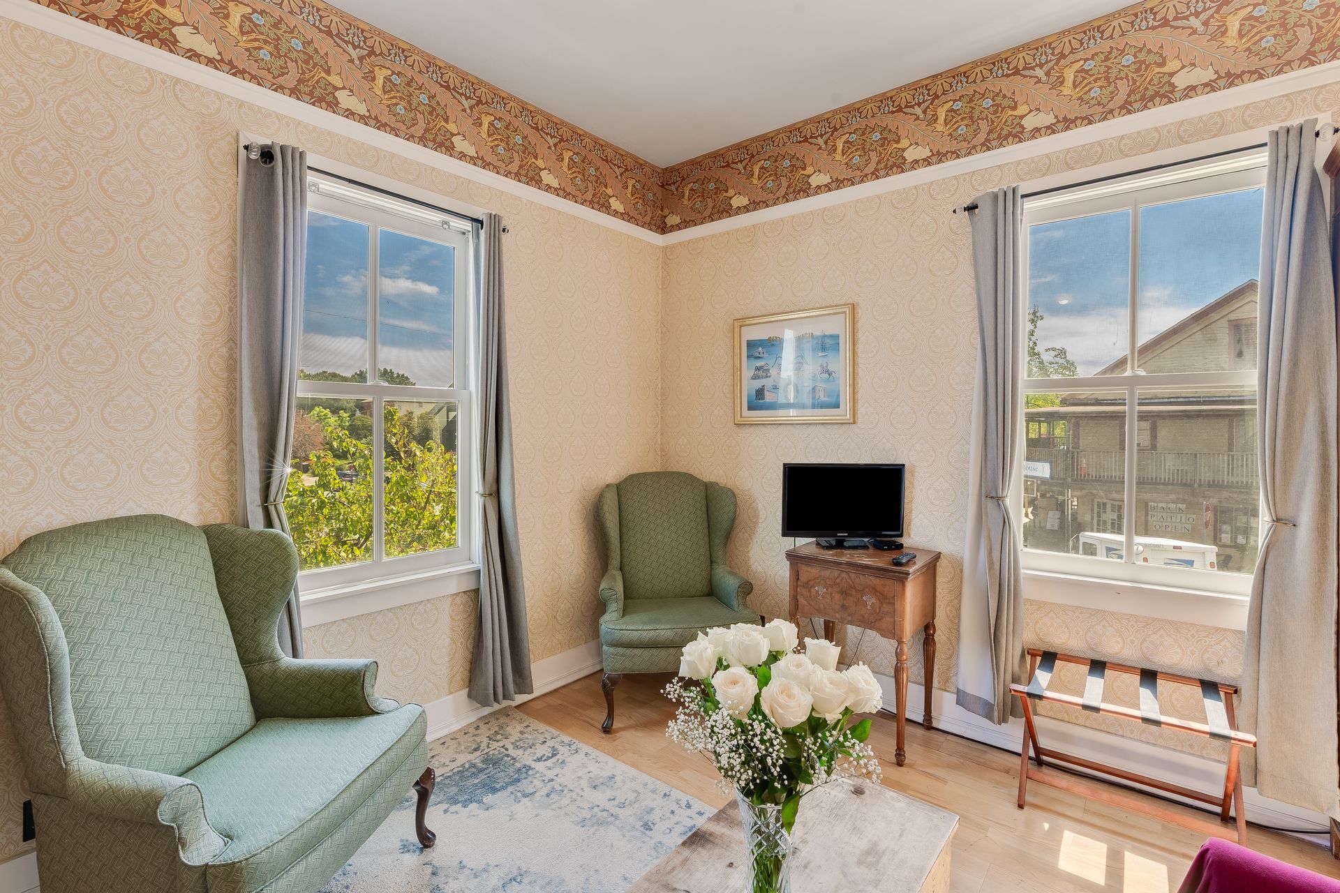 A room with two green armchairs, a bouquet, and two windows with grey curtains.