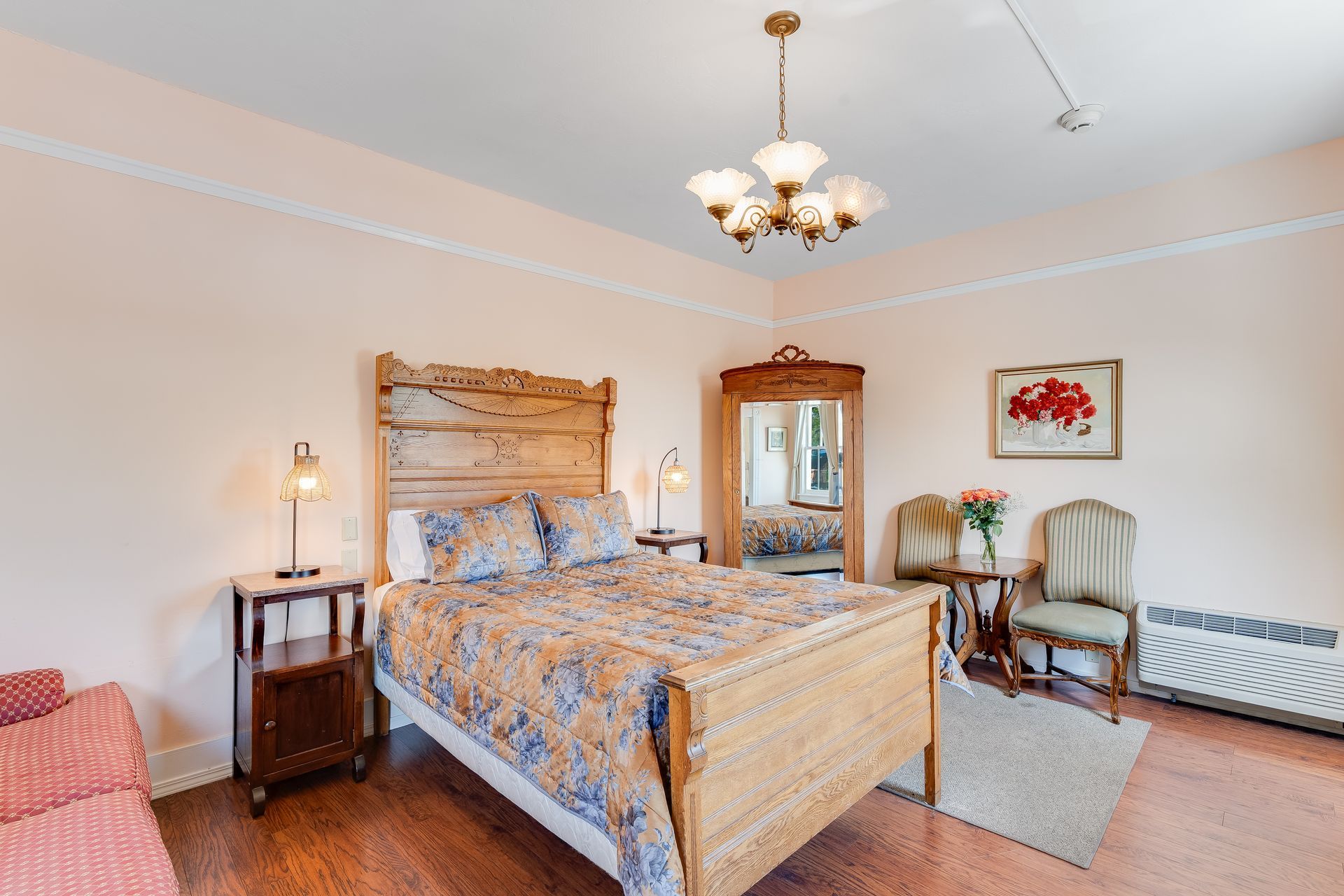 Bedroom with wooden bed, nightstands, and antique furniture. Pale pink walls, hardwood floors.