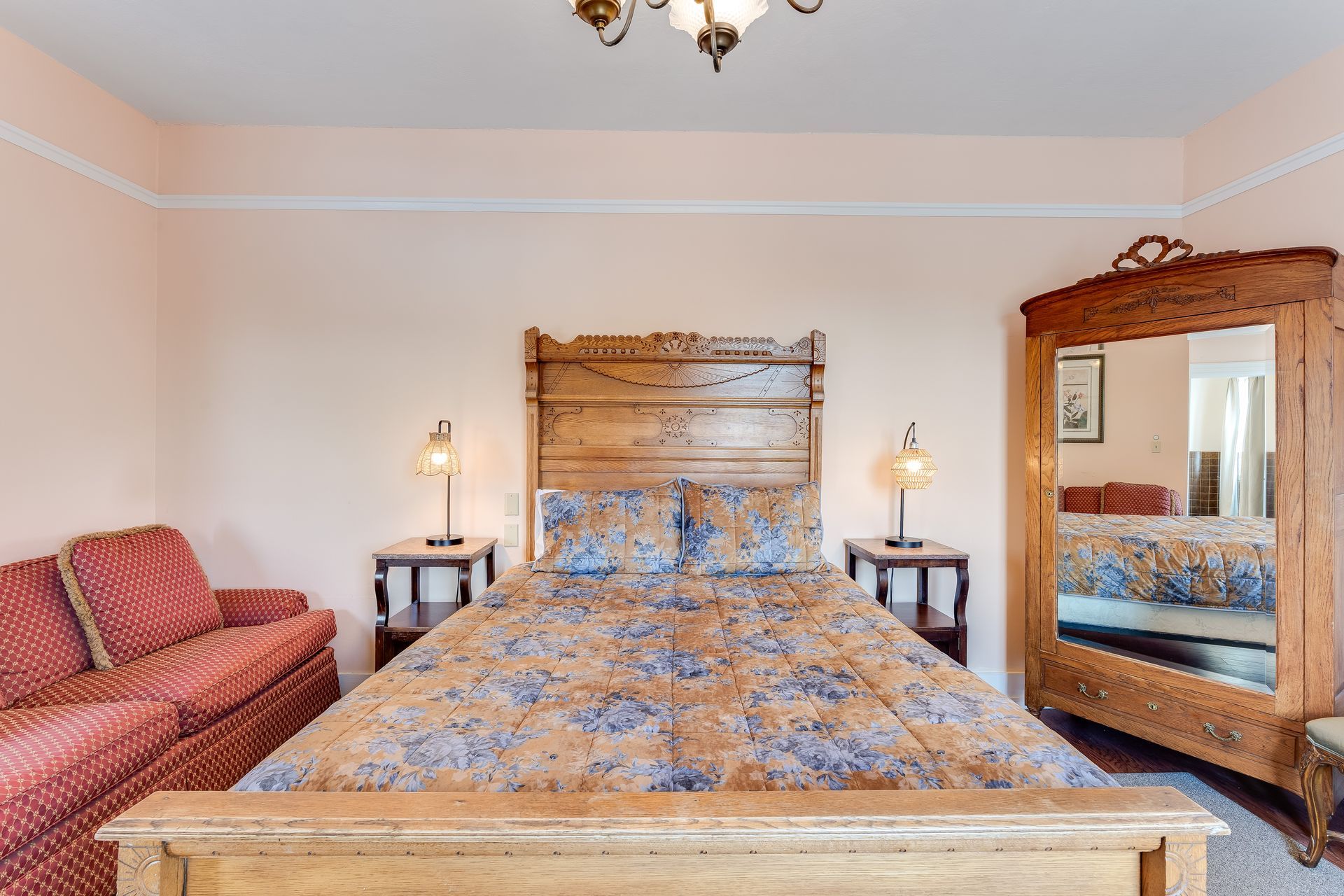 Bedroom with wooden bed, sofa, and armoire. Pink walls and a chandelier.