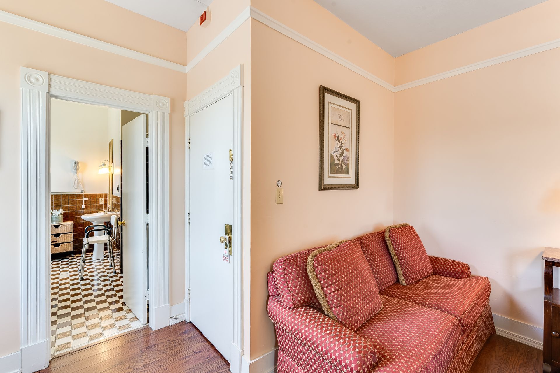Hallway with small red sofa, doorway to bedroom with black-and-white checkered floor. Light peach walls.
