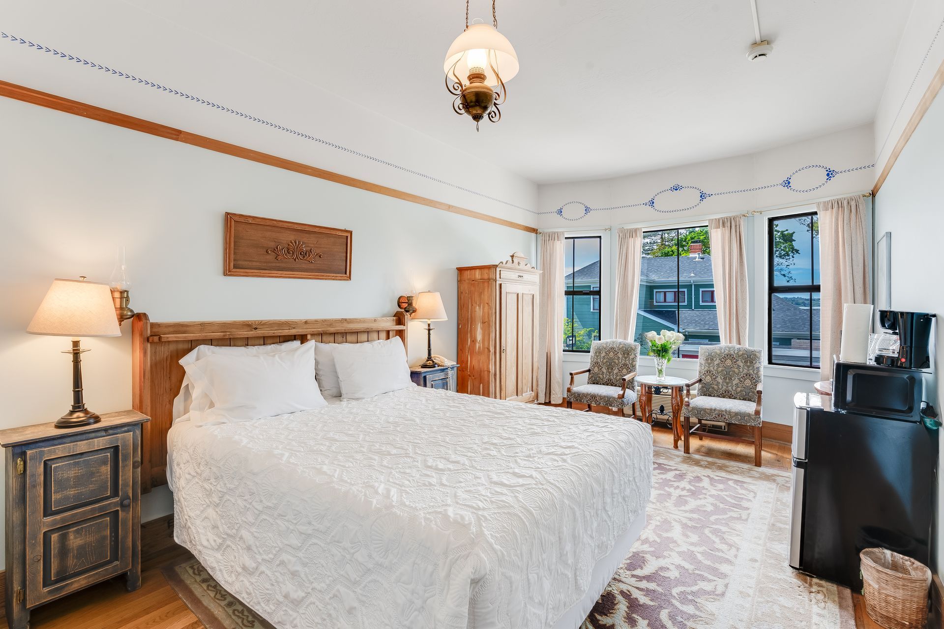 Cozy hotel room with a bed, two chairs near a window, a mini-fridge, and a warm, inviting atmosphere.