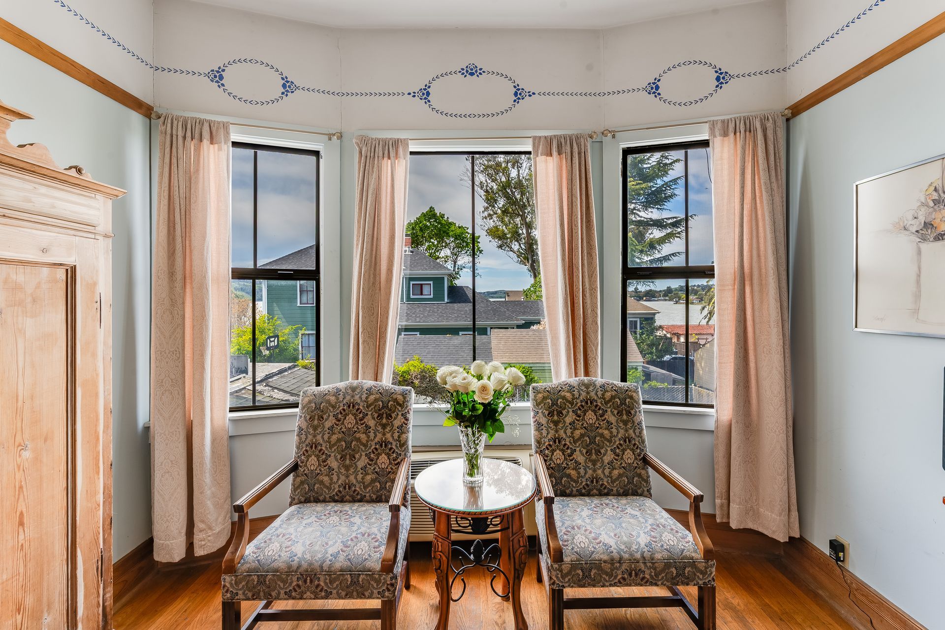 Cozy reading nook with two patterned chairs, round table, large windows with curtains, and painted wall details.