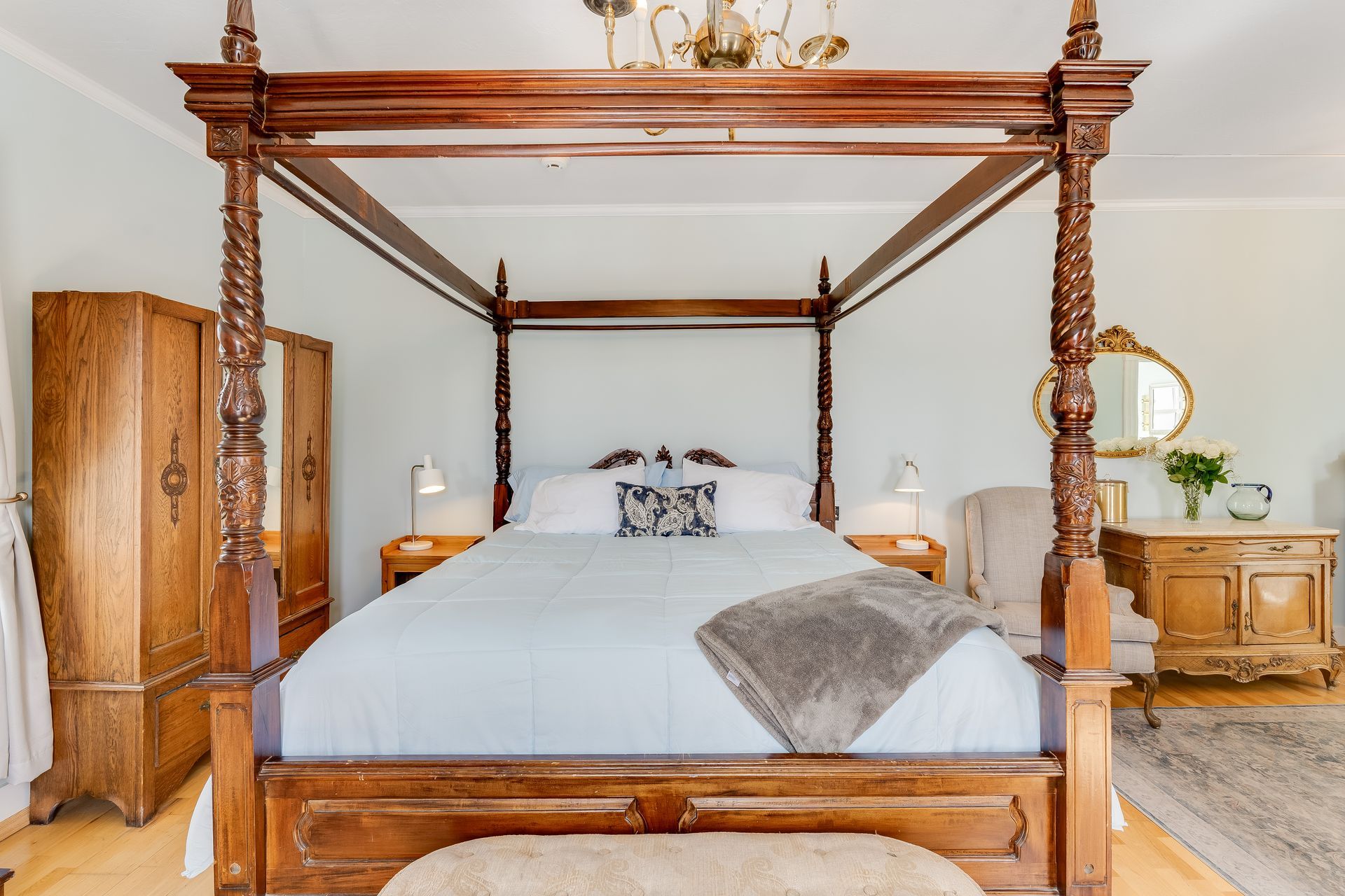Bedroom with a four-poster bed, wooden furniture, and a gold-framed mirror.