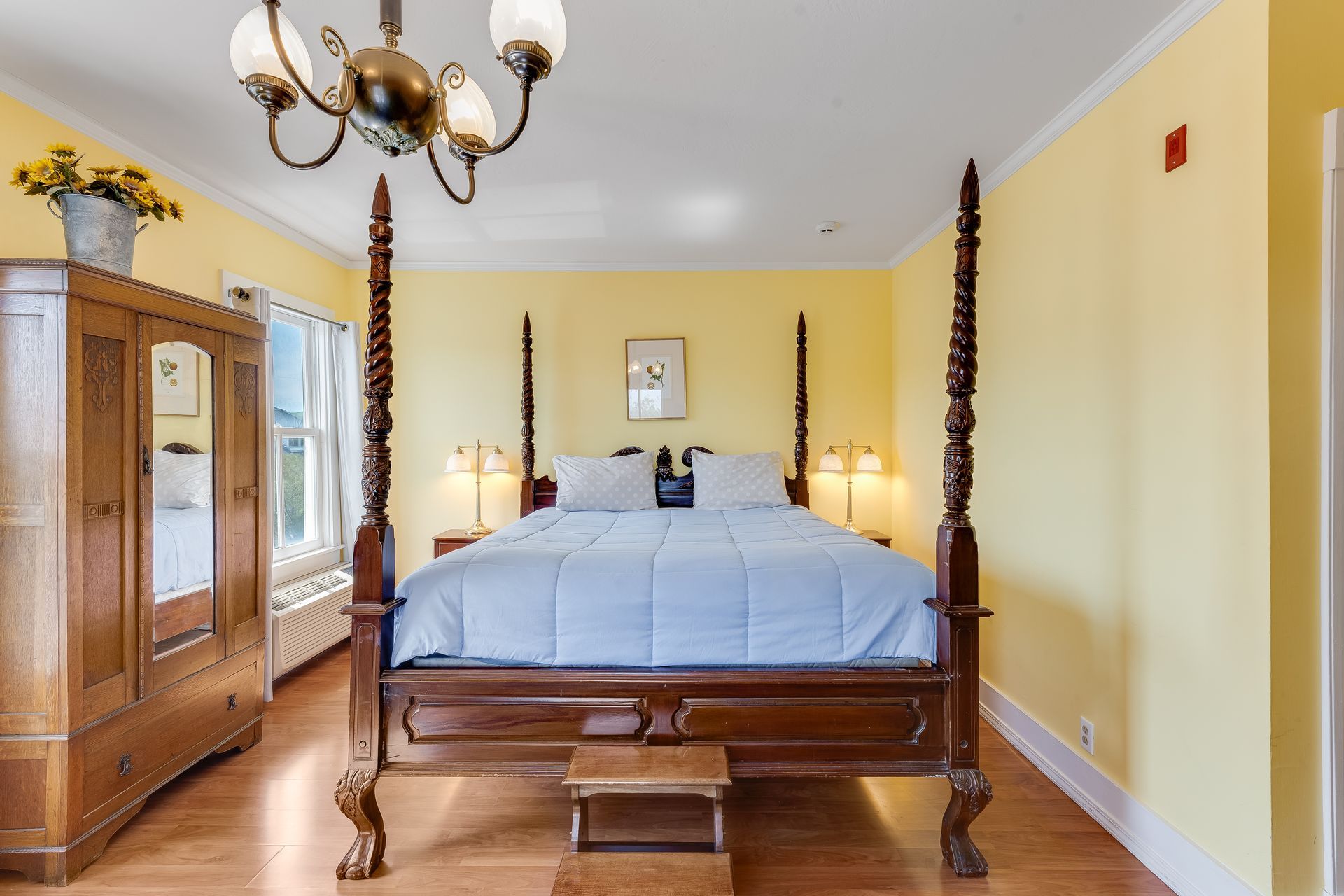 Bedroom with a four-poster bed, antique wardrobe, and yellow walls.