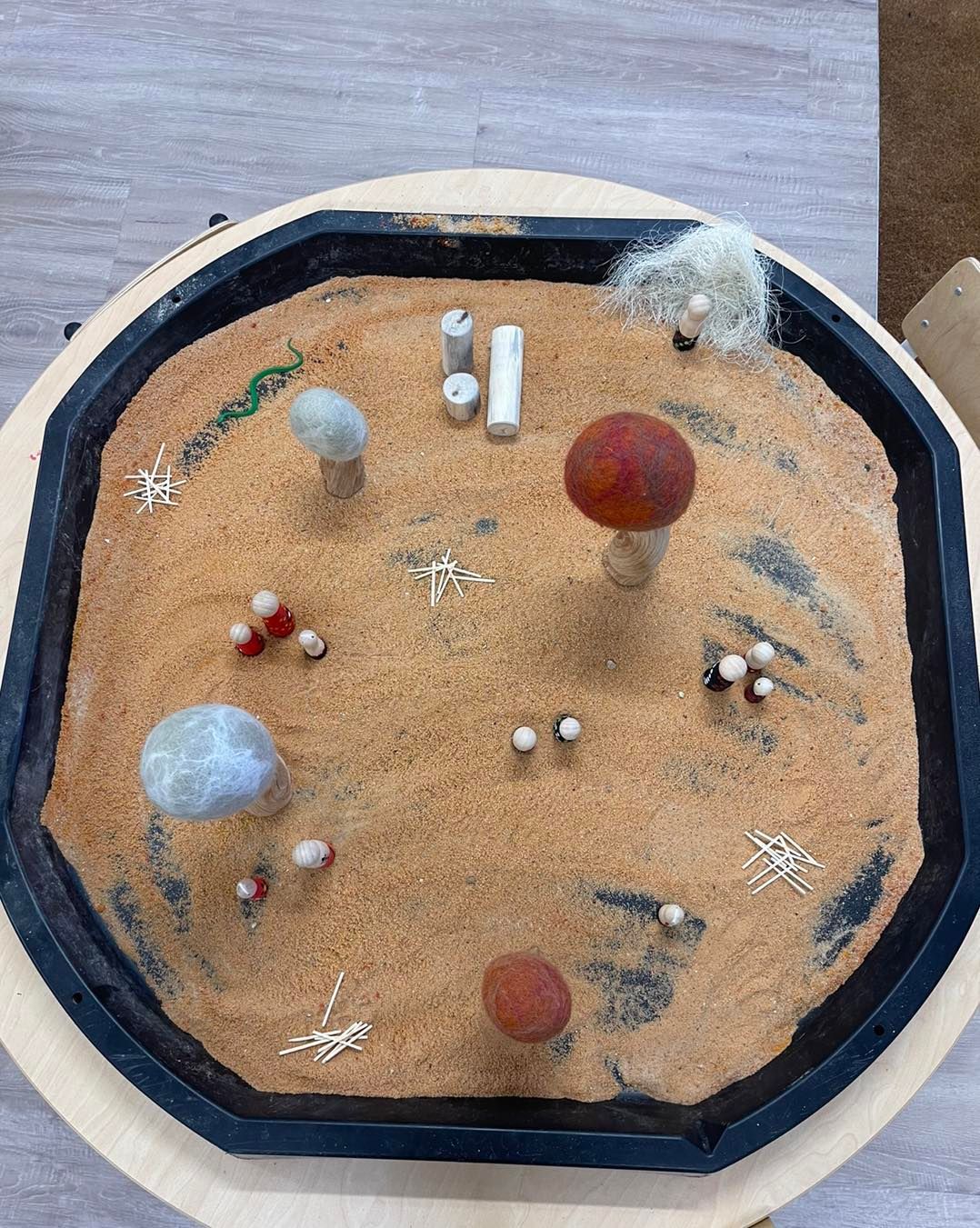 Sand tray with various small objects: mushrooms, stones, and a small felted landscape.