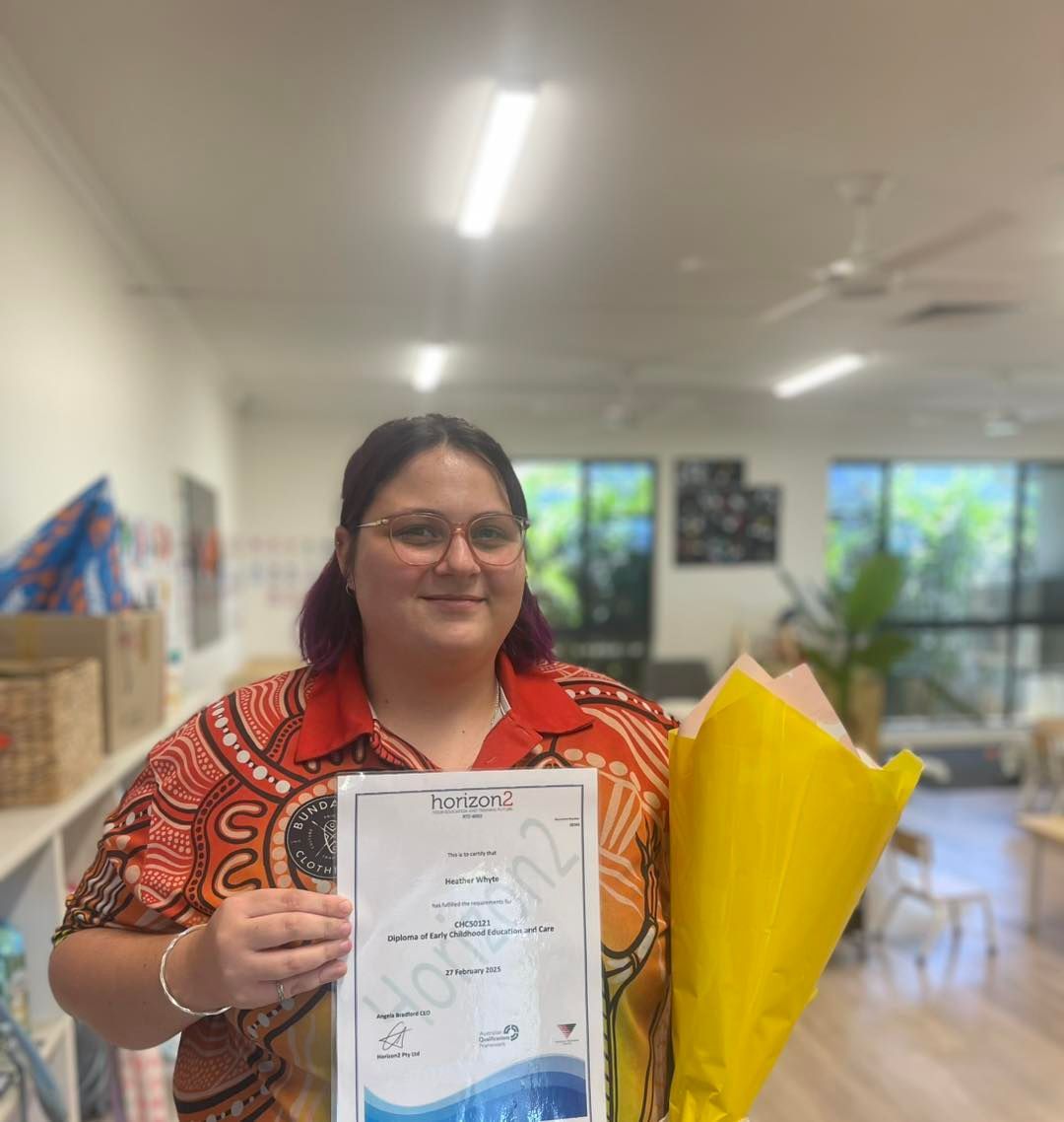 Woman holding a certificate and flowers, smiling in a brightly lit room.
