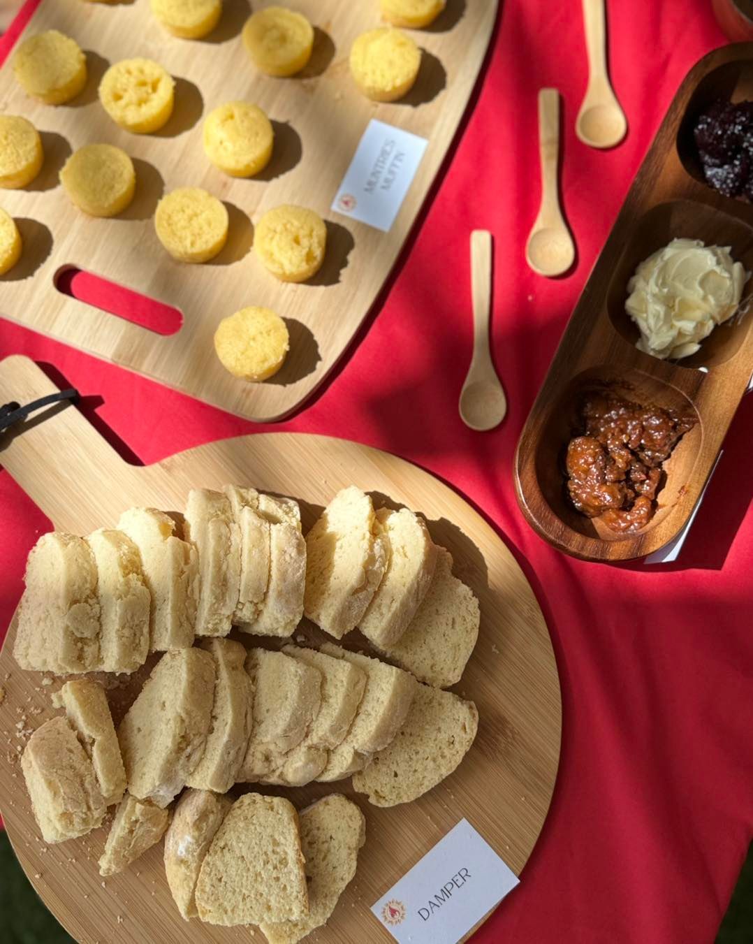Charcuterie spread on red cloth: breads, muffins, and dips on wooden boards with small spoons.