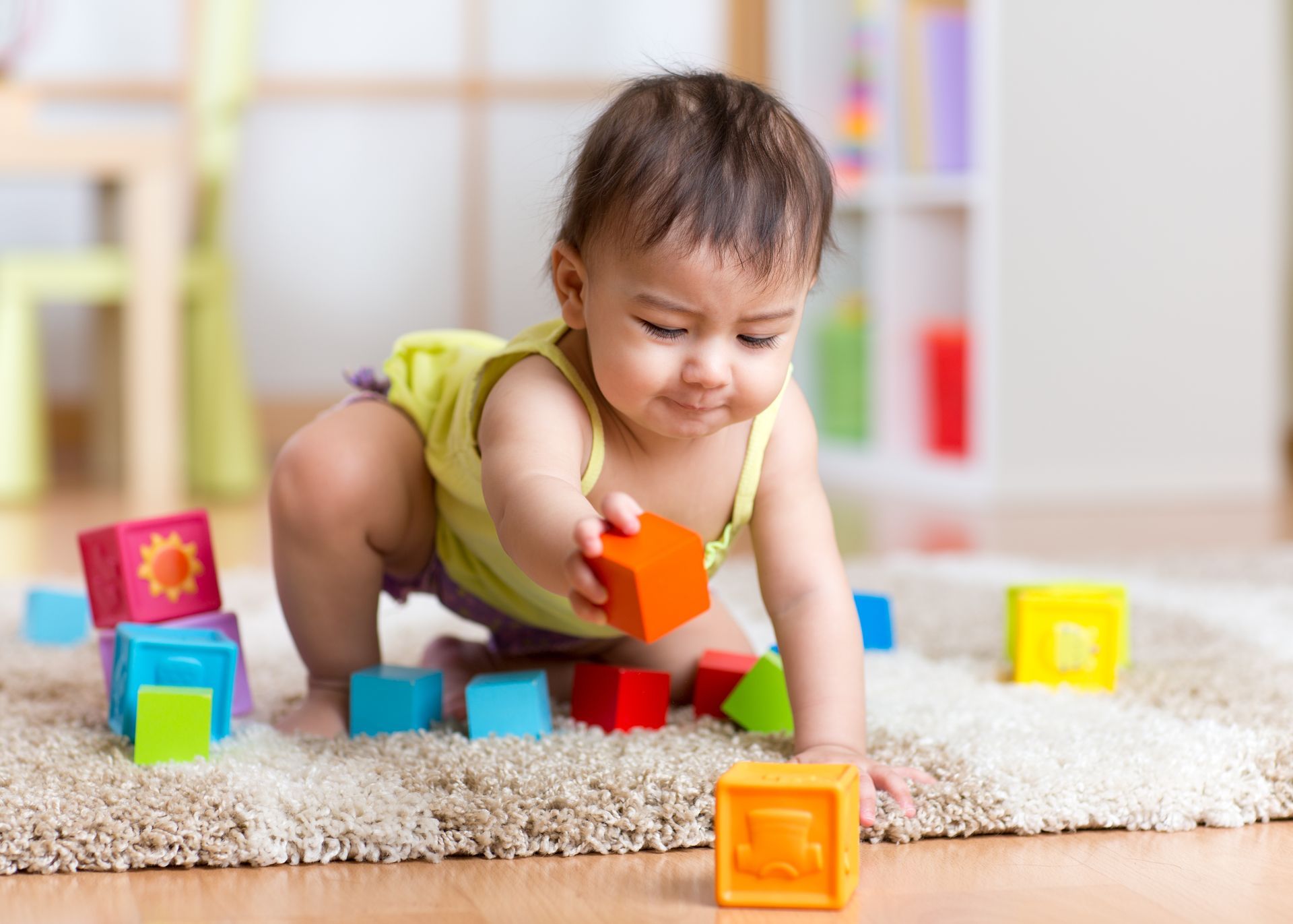 Baby playing with colorful building blocks on a rug.