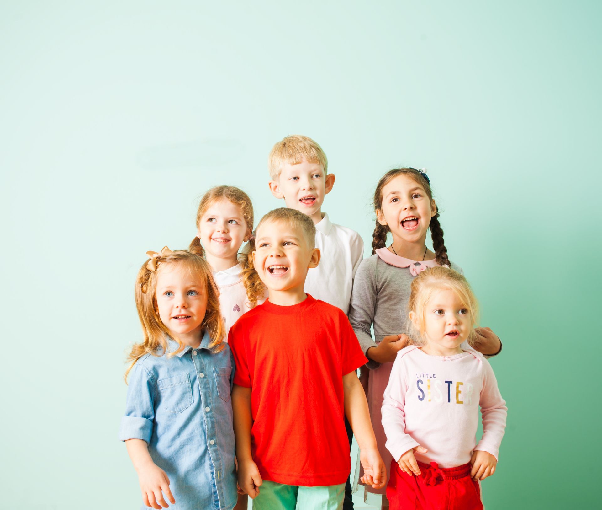 Six children smiling and laughing in front of a light blue background.
