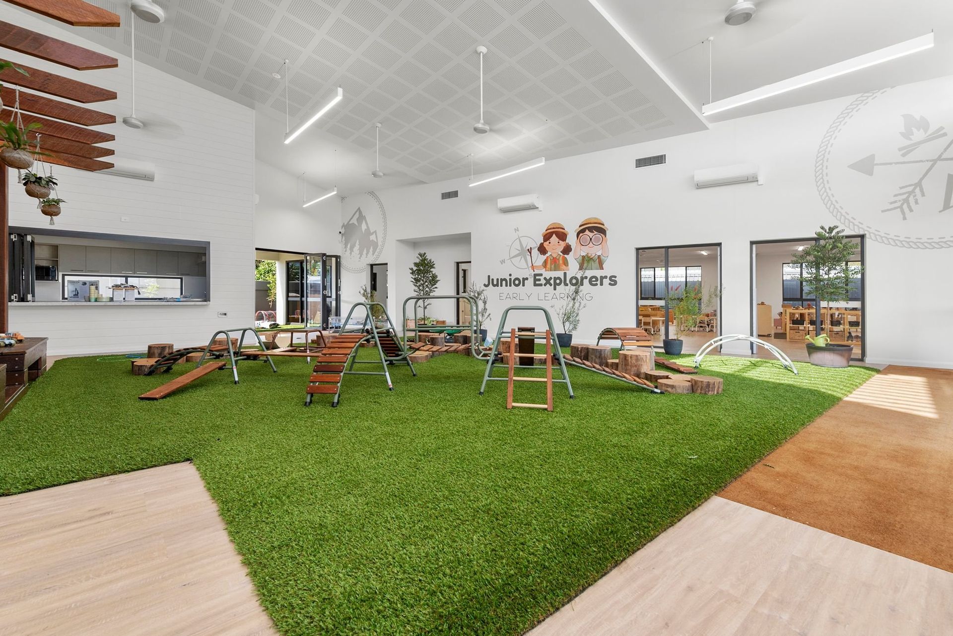 Indoor playground with artificial turf, climbing structures, and open play area for children.