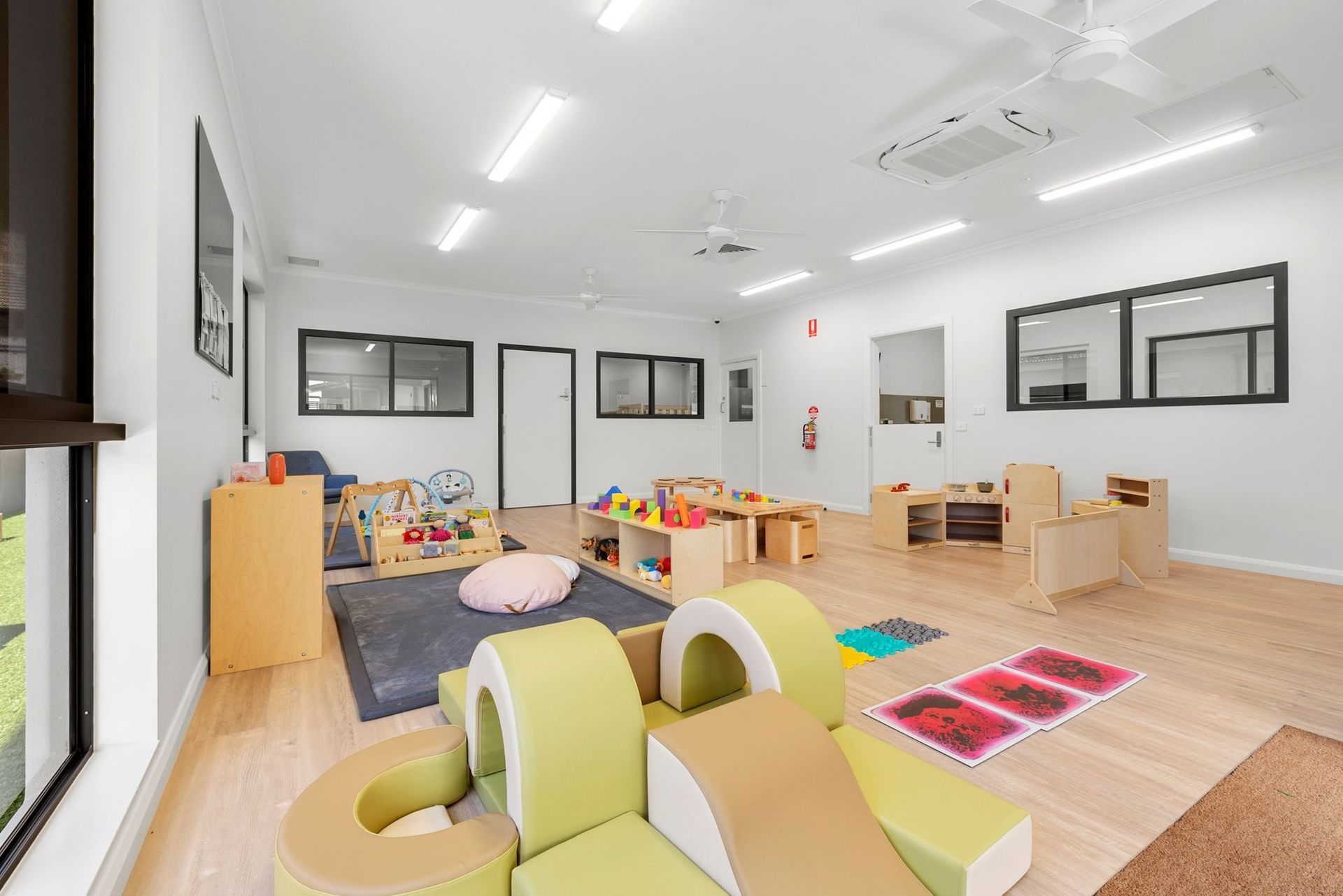 Bright playroom with wooden floors, low play structures, toys, and natural light.