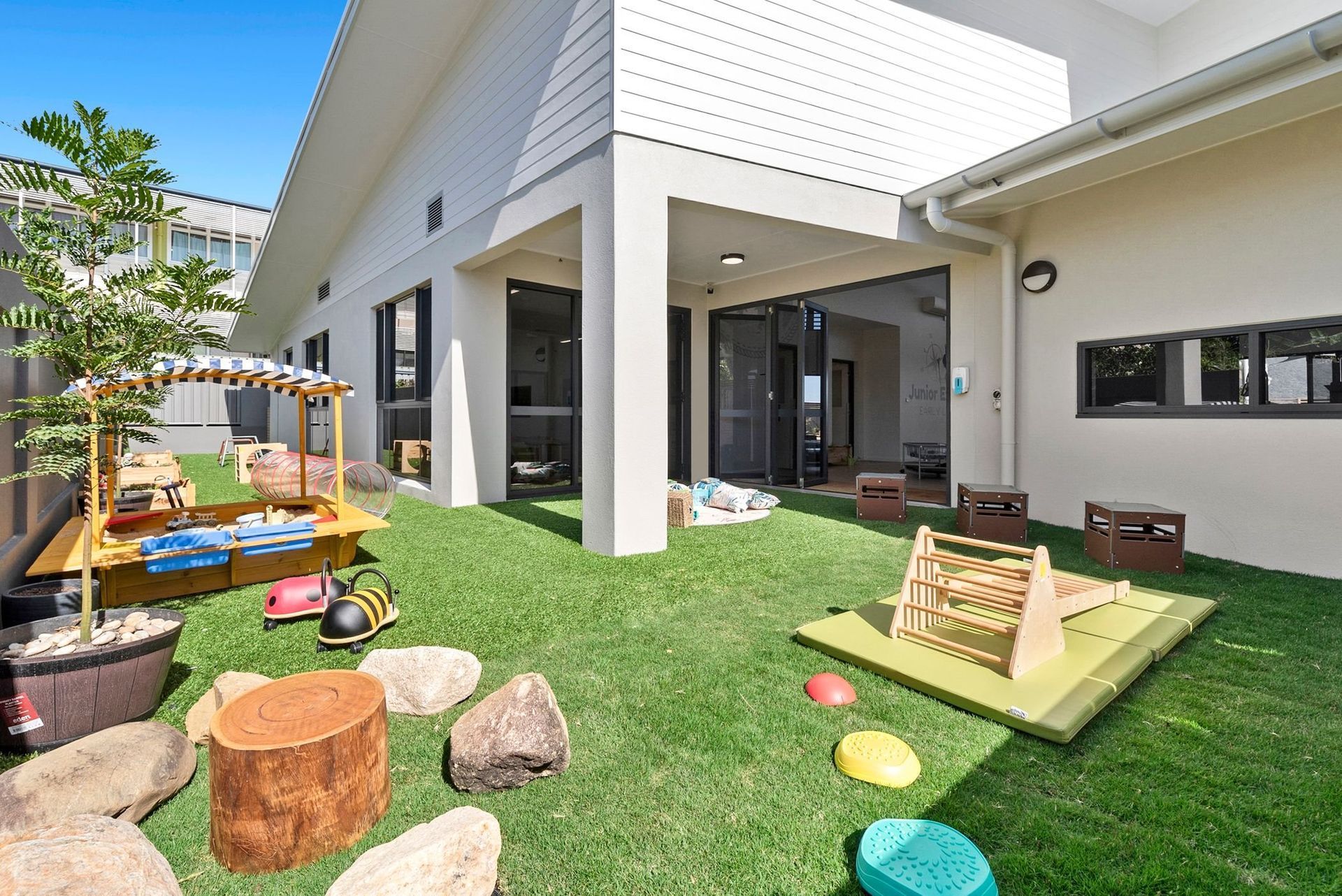 Outdoor preschool play area with artificial grass, toys, and covered structure.