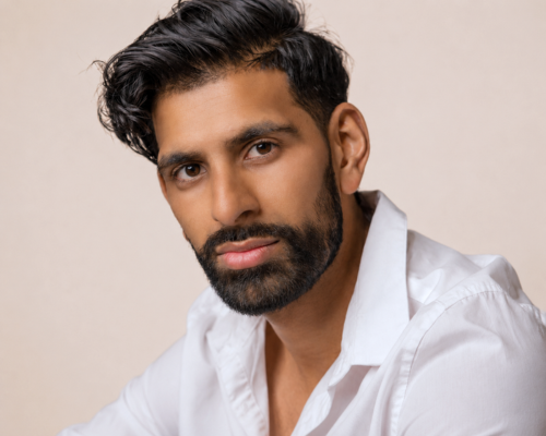Portrait of a person with curly hair wearing a dark shirt against a plain beige background