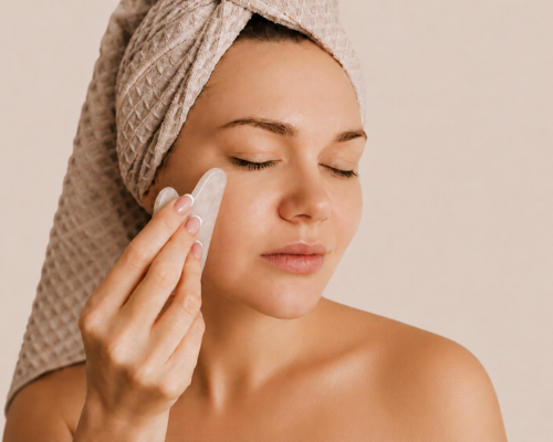 Person applying skincare with a cotton pad, wearing a towel turban in warm indoor light