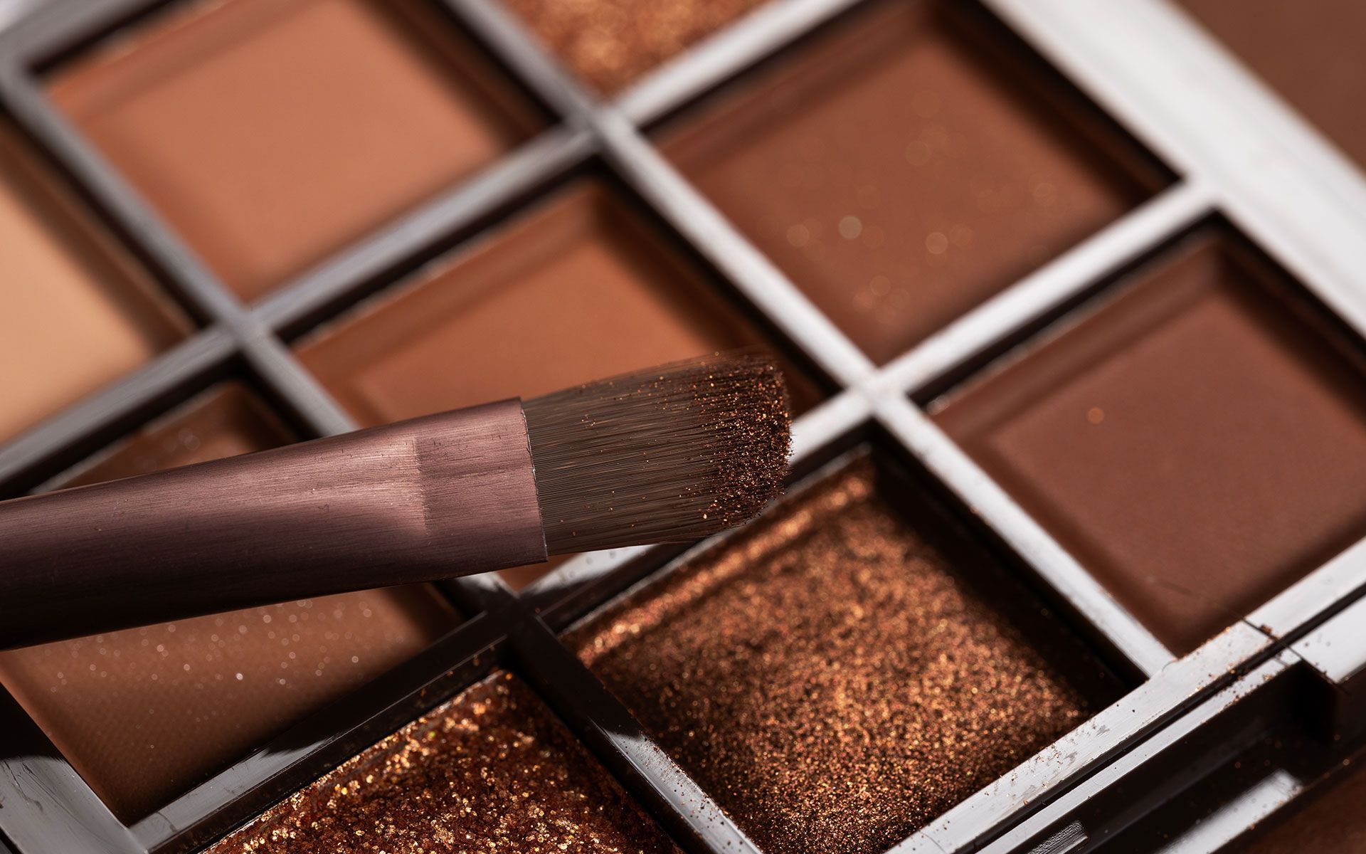 Eyeshadow palette with warm brown shades and a makeup brush applying glittery bronze shadow