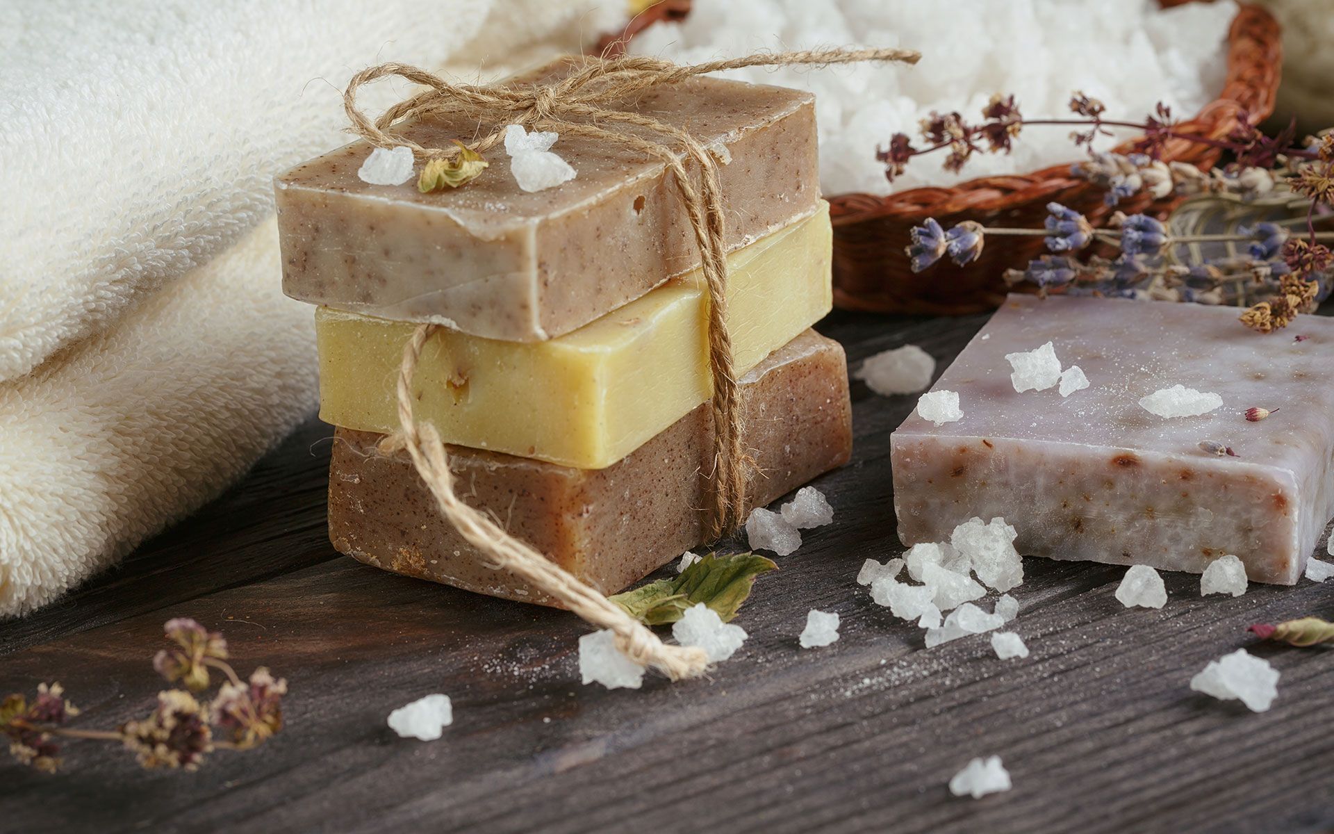 Stacked handmade soap bars with dried flowers and coarse salt on a rustic wooden surface