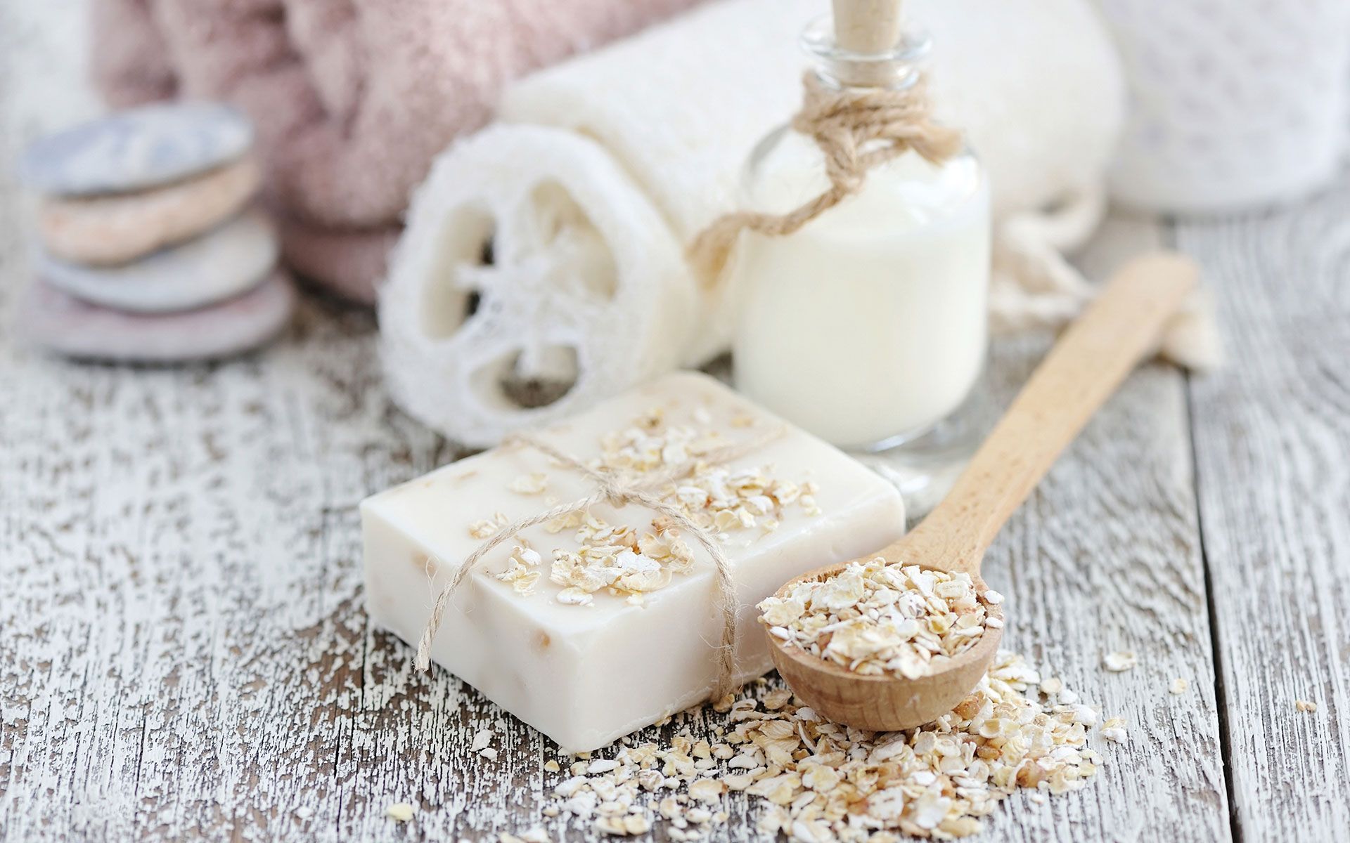 Spa items with white soap bars, a jar candle, loofah, and towels on a light wooden table