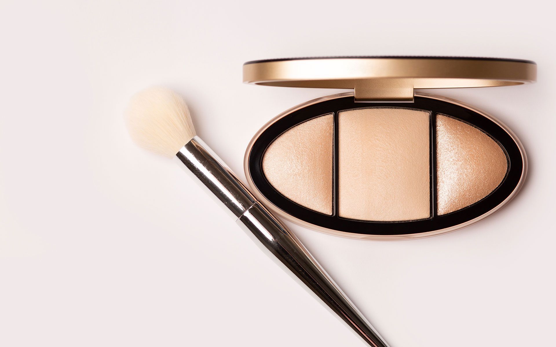 Open gold eyeshadow compact with brush on a pale pink background